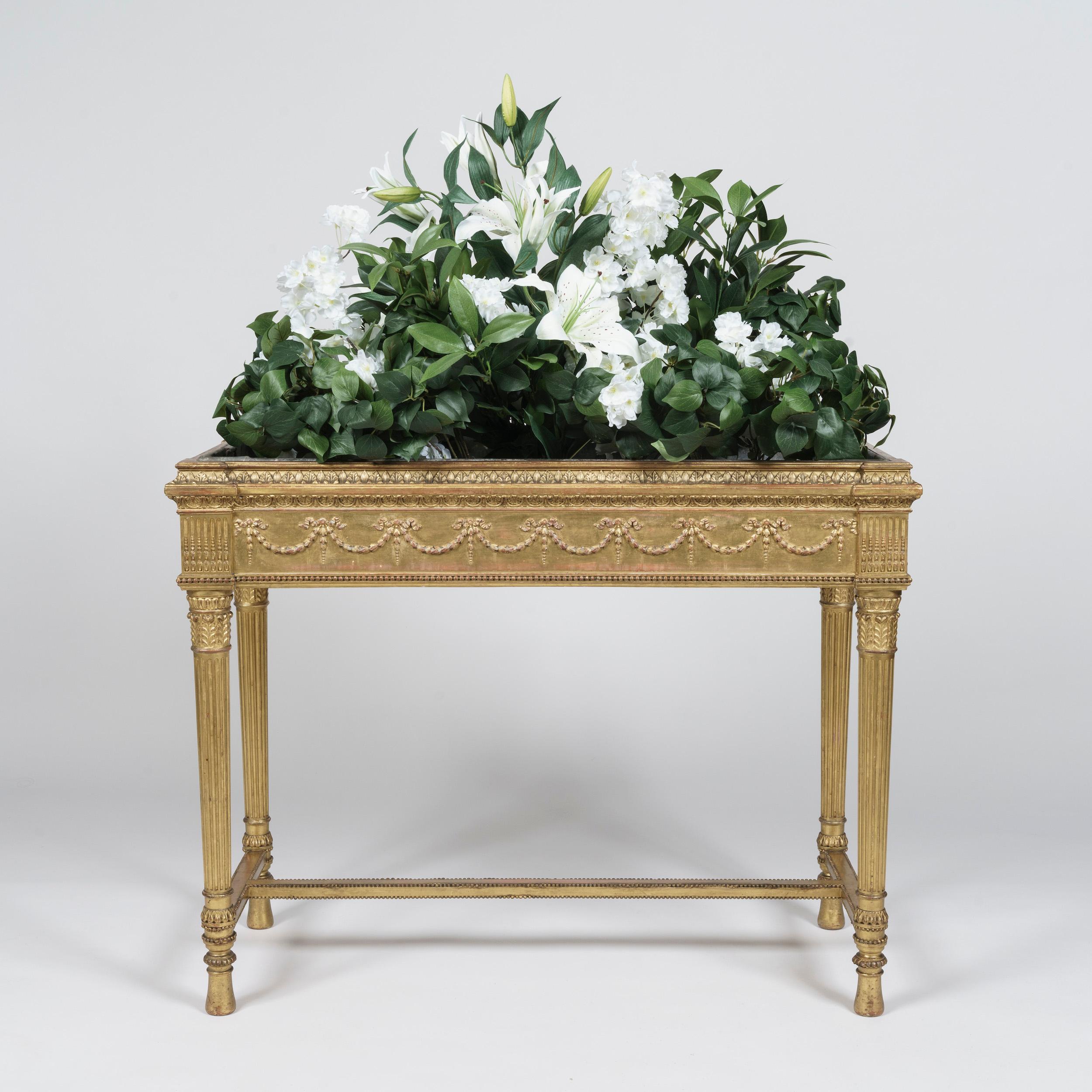 A pair of neo-classical
Giltwood Jardinières

Carved with refined detail and finished with gold leaf water-gilding, the fluted tapering legs joined together with a beaded H-stretcher, the acanthus-carved capitals supporting the zinc-lined