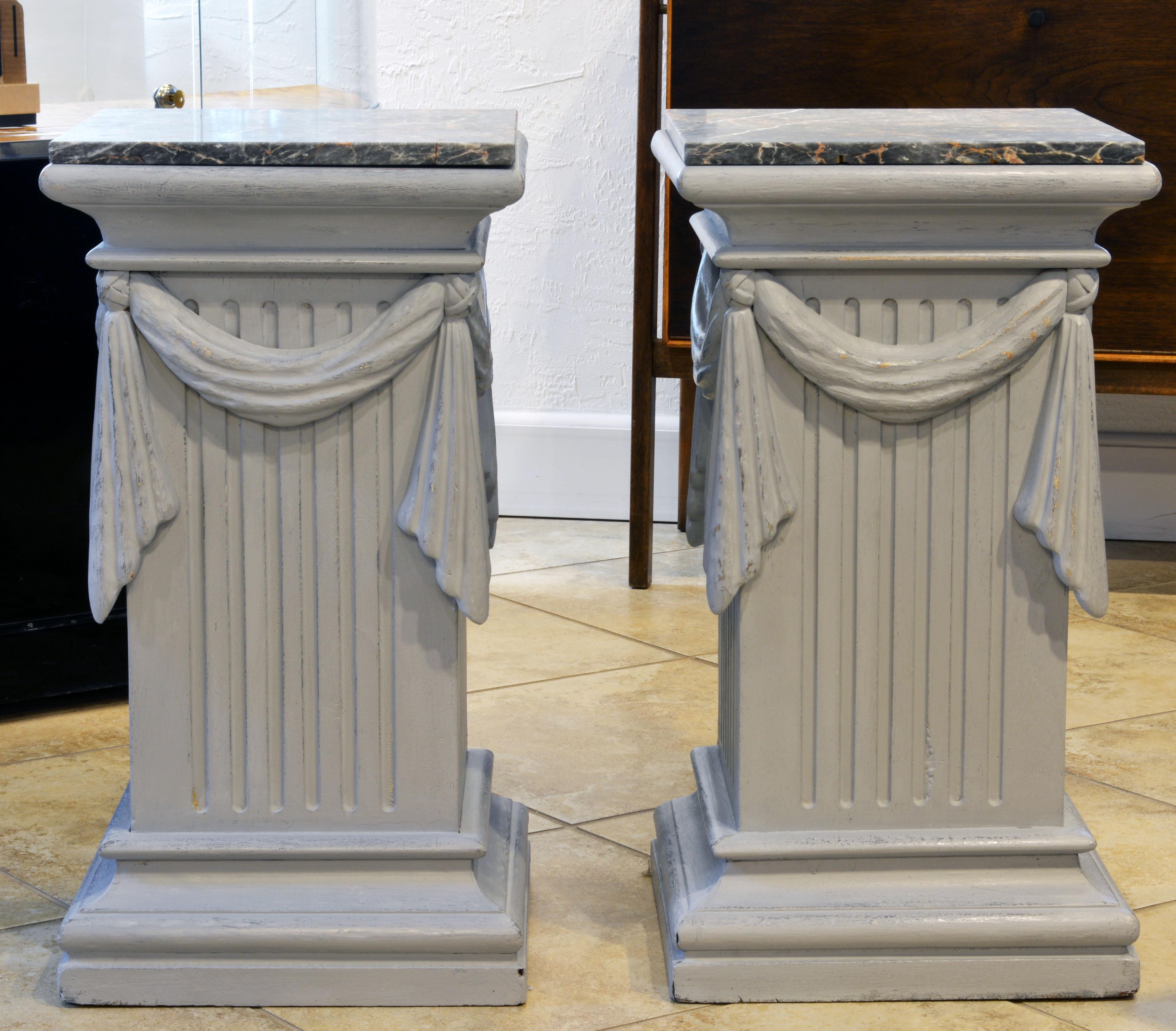 This pair of neoclassical Gustavian style carved and gray painted pedestals are equally useful as lamp tables or end tables. They feature antique marble tops above molded cornices, fluted sides decorated by swags continuing all around and rest on