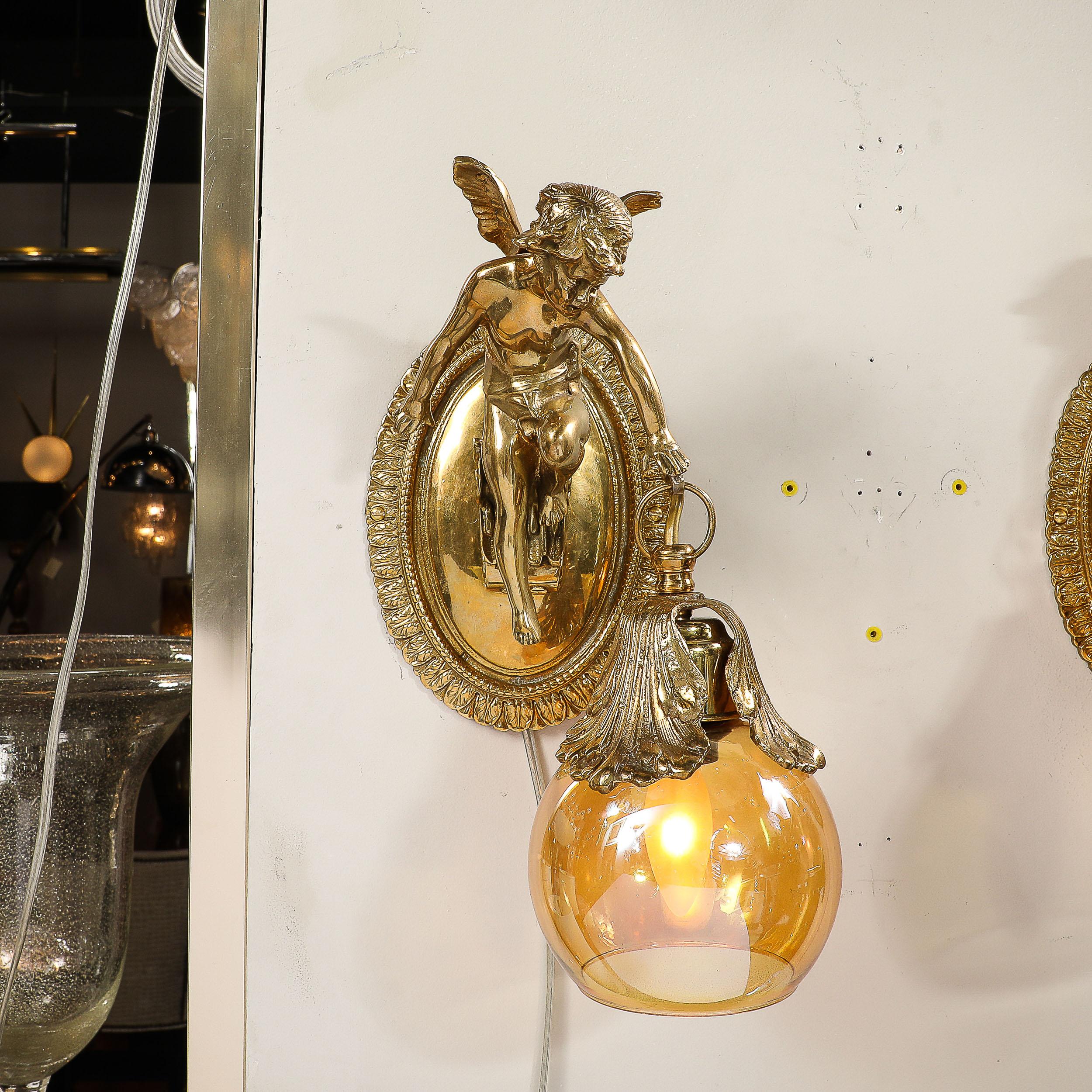 This exquisite Pair of Neoclassical Cherub Sconces in antique Brass W/Smoke Amber Shades originates from the Czech Republic during the latter half of the 20th Century. Featuring a lovely neoclassical sculpted figure of Winged Cherubs extending from