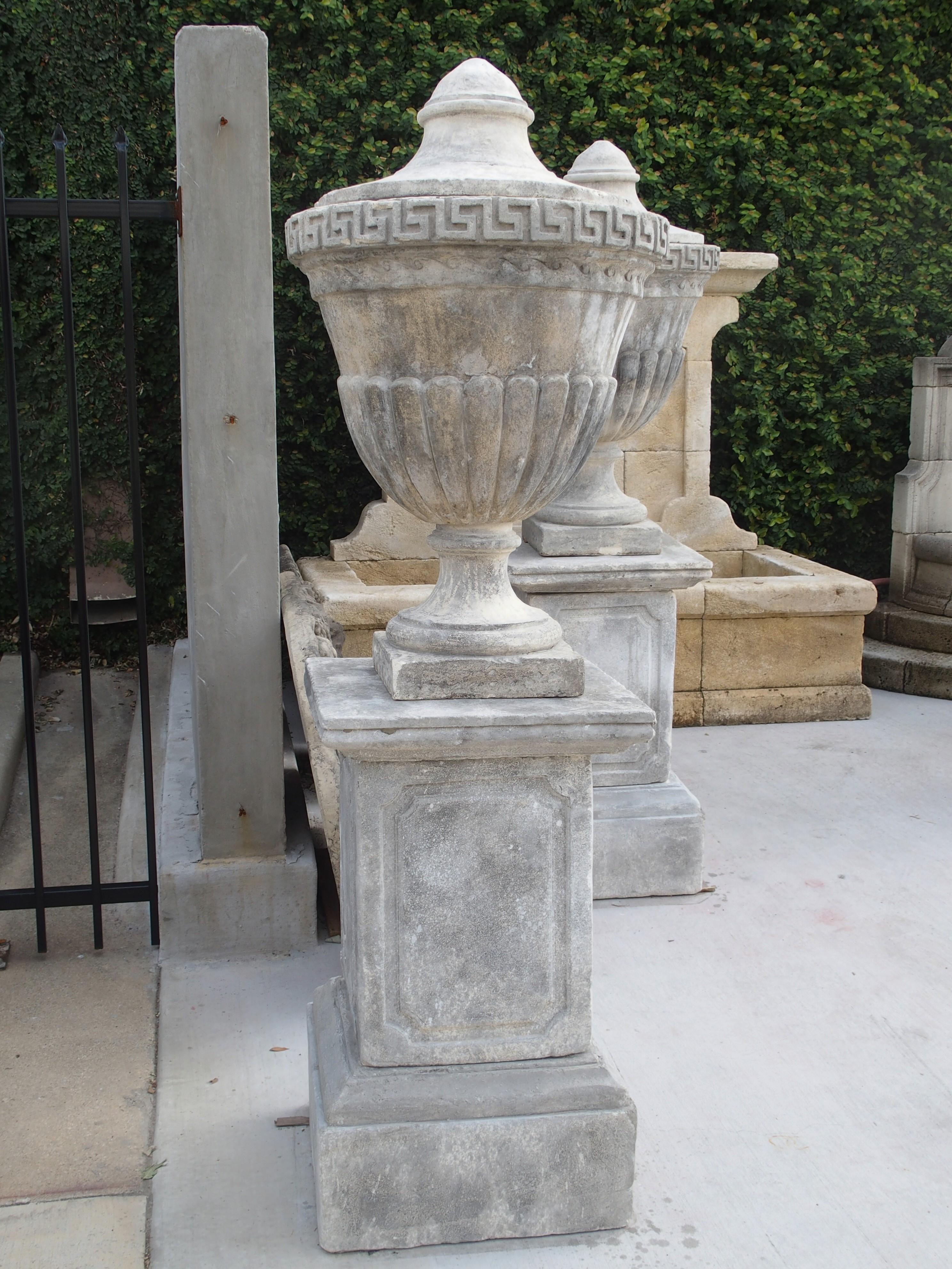 This pair of composition limestone urns on pedestals from Southern Italy Stand at six feet tall.

The body of the urns are decorated with several elements of Neoclassical motifs. Neoclassicism was inspired by the art and culture of ancient