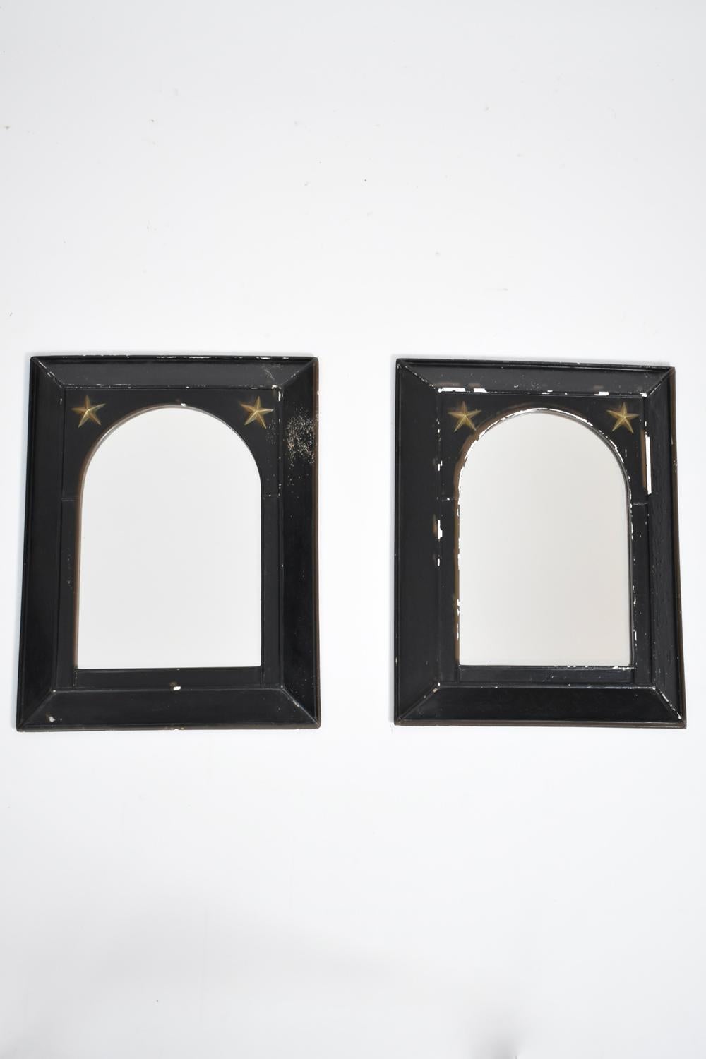 Pair of neoclassical rectangular mirrors with frames rounded view and protruding profile in black lacquered wood, the upper part flanked by two brass stars. France, 1960s.