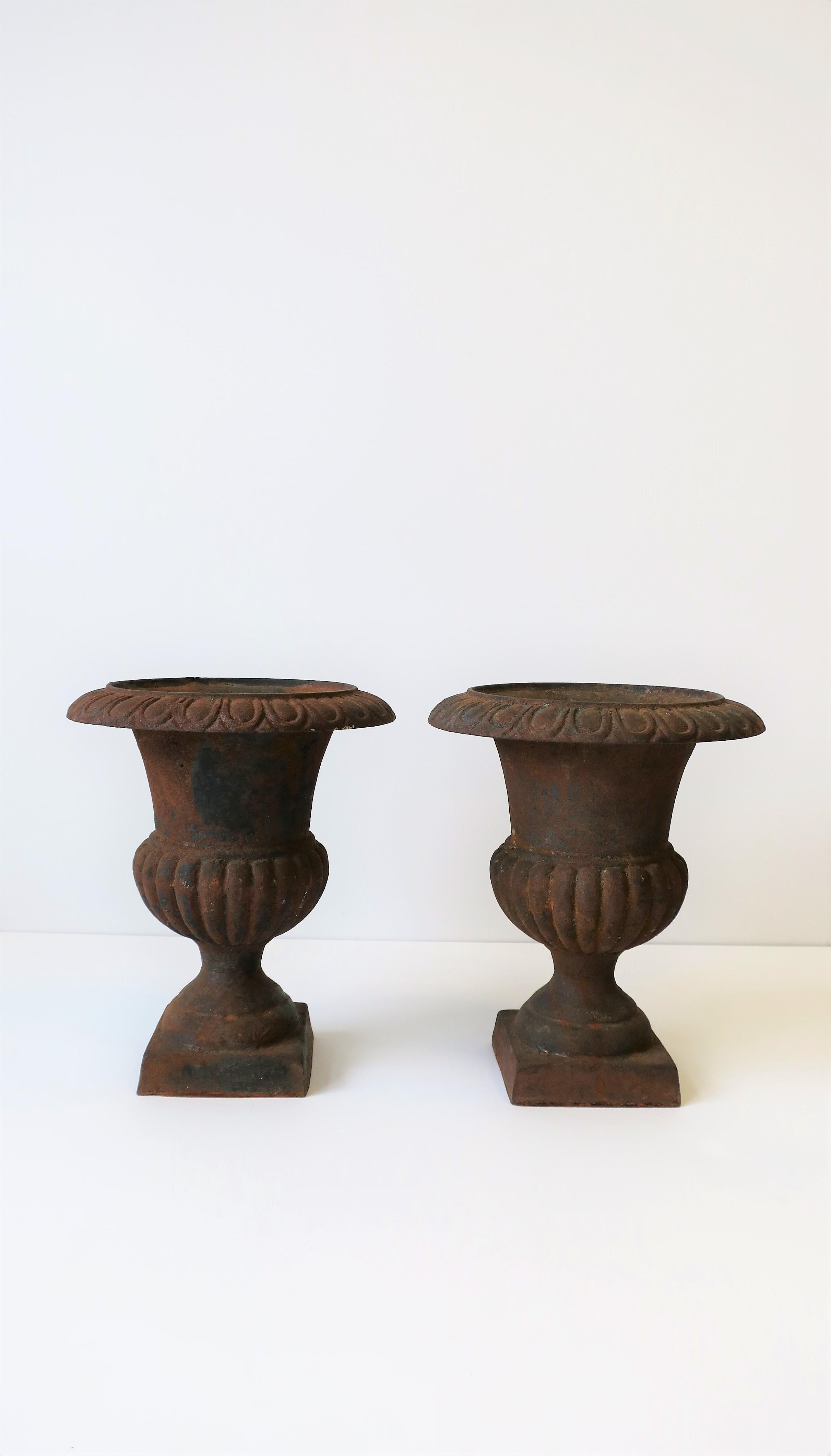 A beautiful pair of weathered iron urns plant or flowerpot cachepot jardinieres with square pedestal bases in the Neoclassical style, circa 20th century, maybe Europe/France. Substantial in weight, use indoors or outdoors garden, patio, etc. Pair