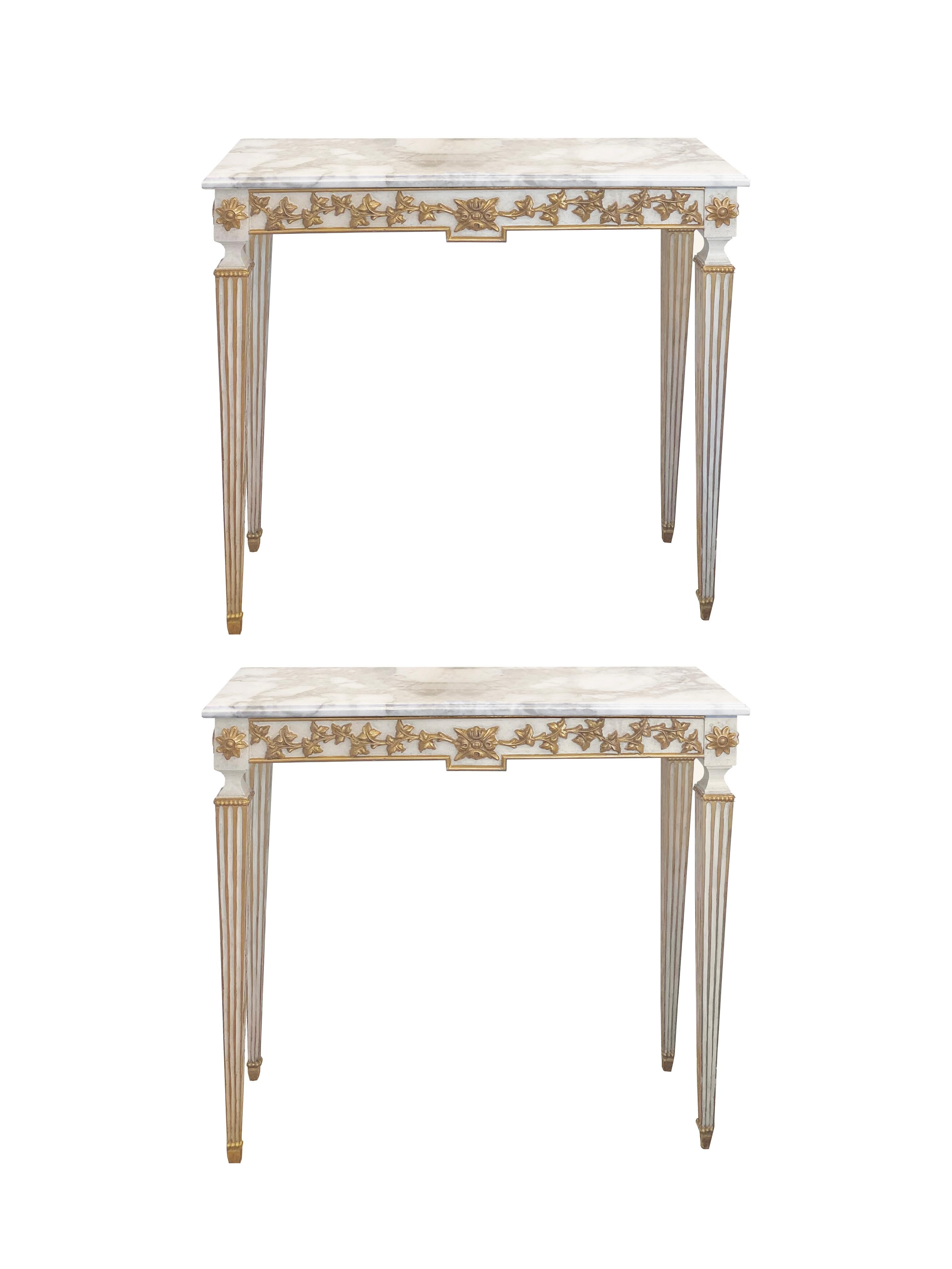 A pair of antique neoclassical Italian marble and gilt-painted marble console tables. Parcel gilt relief carved foliage is featured on tapering fluted legs, each with a white variegated marble top. We recommend using child-safe or earthquake