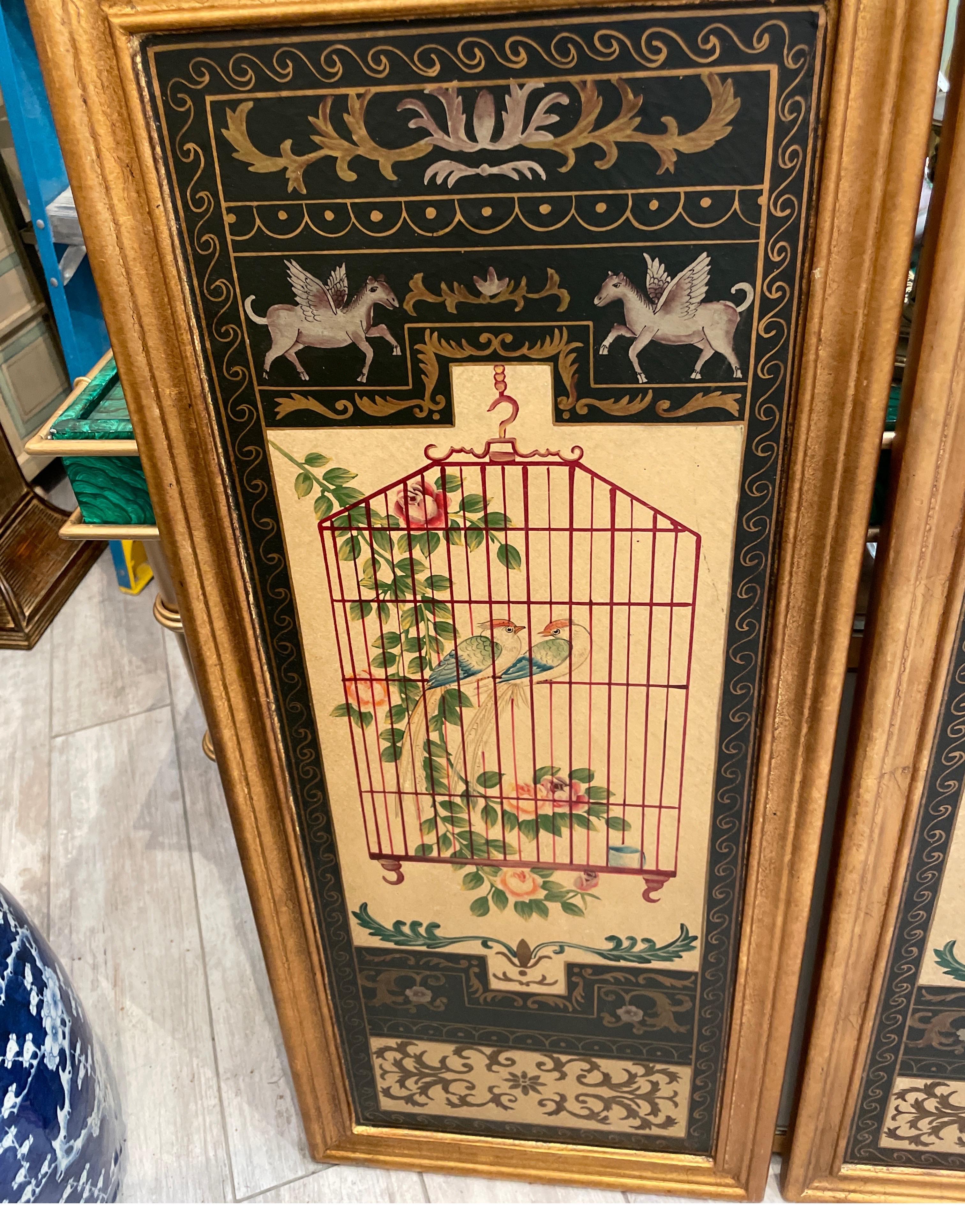 Zwei klassizistische Wandtafeln im Vintage-Stil, die gegensätzliche Vögel in ihren Käfigen, umgeben von Laub, darstellen. Sie sind auf Holzplatten mit vergoldetem Rahmen.