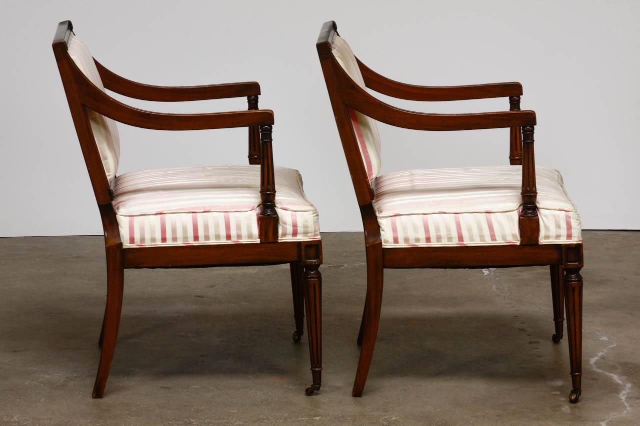 Elegant pair of neoclassical armchairs or fauteuils made in the French Louis XVI taste. Features carved mahogany frames with a square back and graceful sweeping arms. The backrest is decorated with small brass rosettes on the corners. The arm