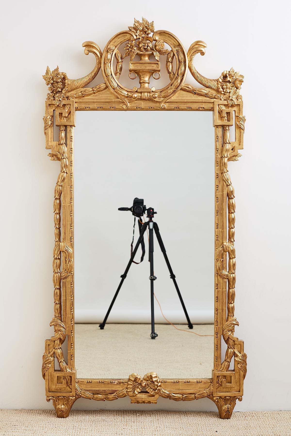 Grand pair of French Louis XVI style giltwood pier mirrors or mantle mirrors made in the neoclassical taste. The rectangular mirrors are decorated with large Greek key designs on each corner and draped by laurel swag ropes with acanthus leaves. The
