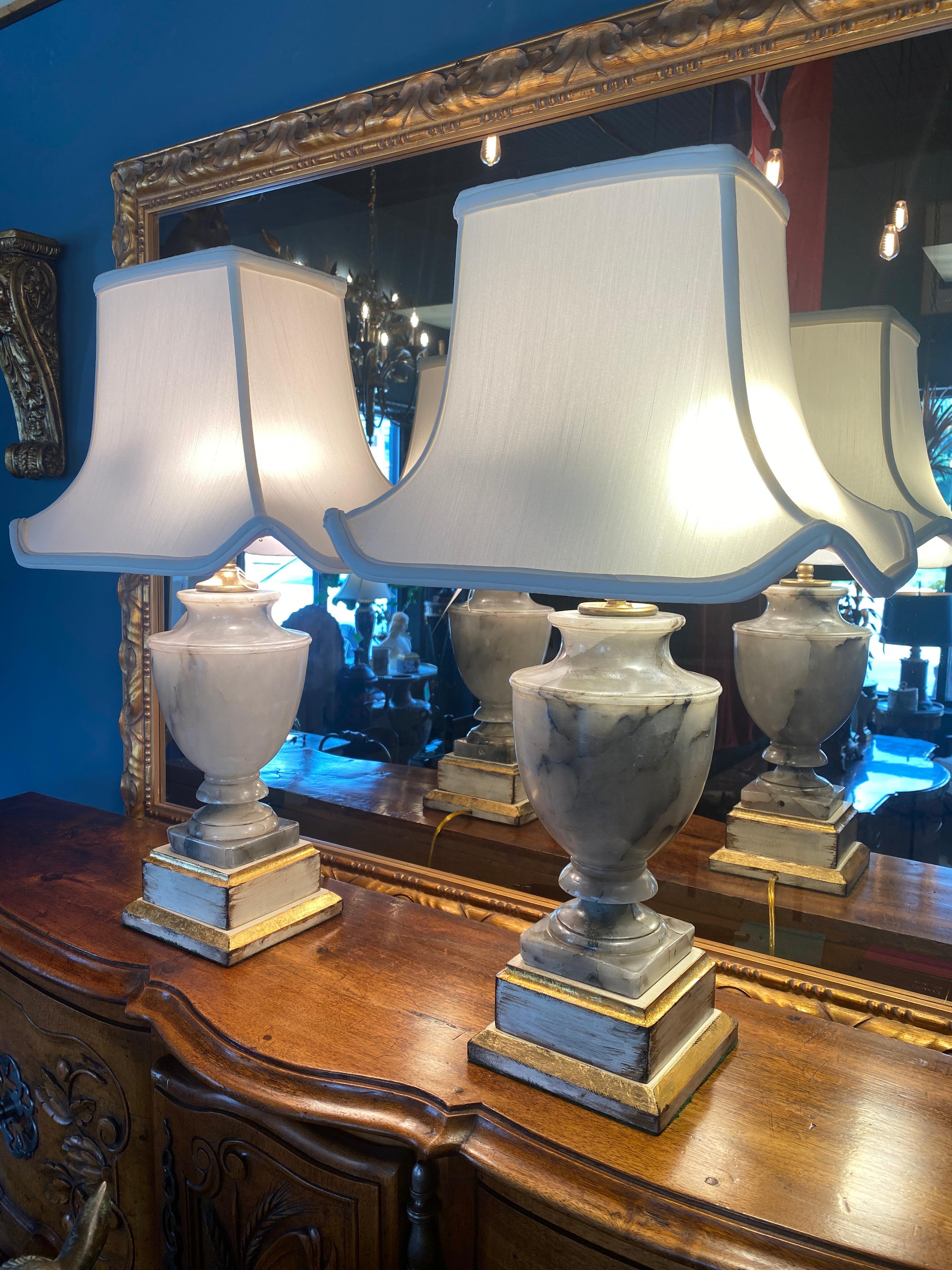 A pair of carved Oynx Urn form lamps mounted on lacquer and gilded Mahogany bases, new wiring. Pagoda lamp shades. Two horizontal sockets with pull cords in each lamp. Brass posts and finials. Bases are lined with felt on the bottoms. 

Measures: