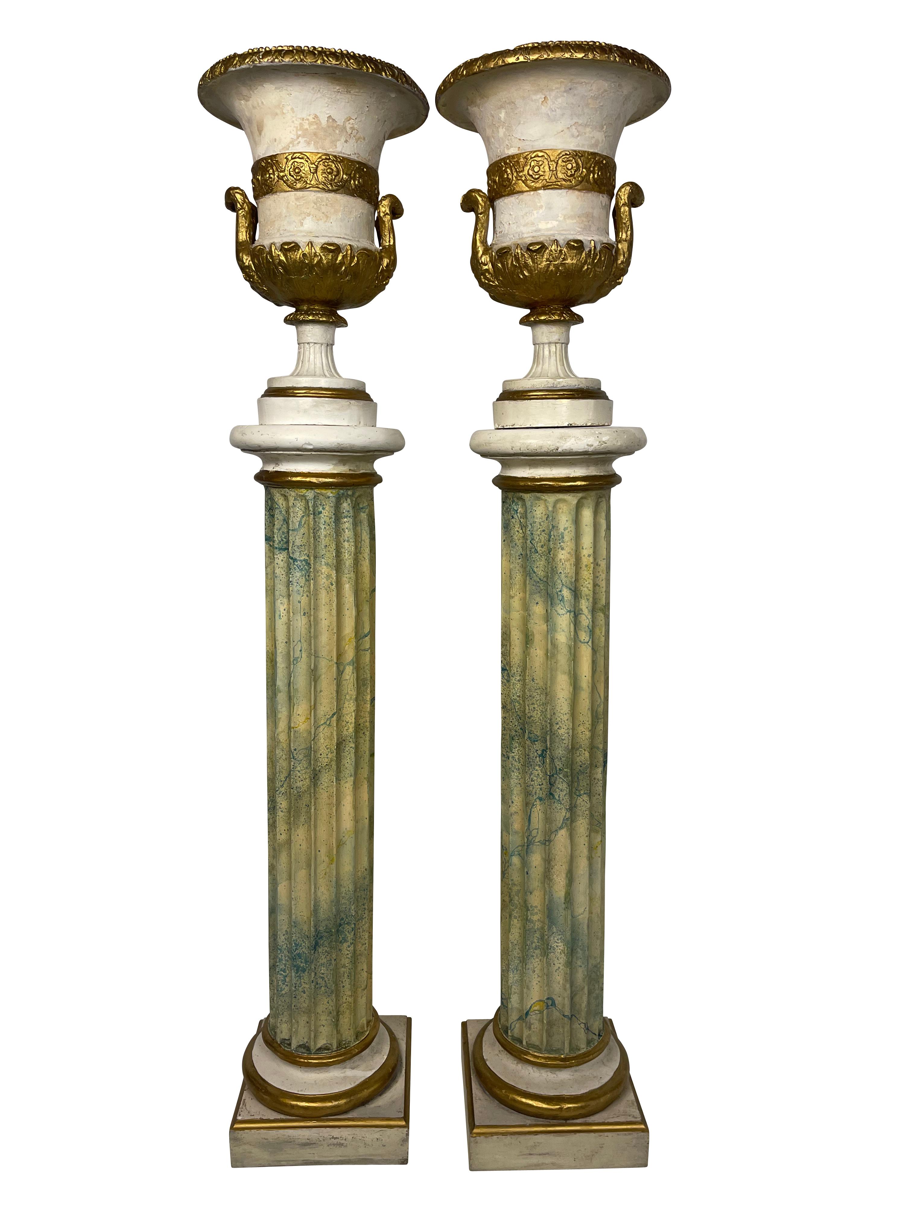 A decorative and useful pair of classical urns composition planters on stands. The urns are of woods and plaster with gilt accents. The blue./green reeded columns are faux marble with gilt accents as well. Both urns are lined in plastic for use with