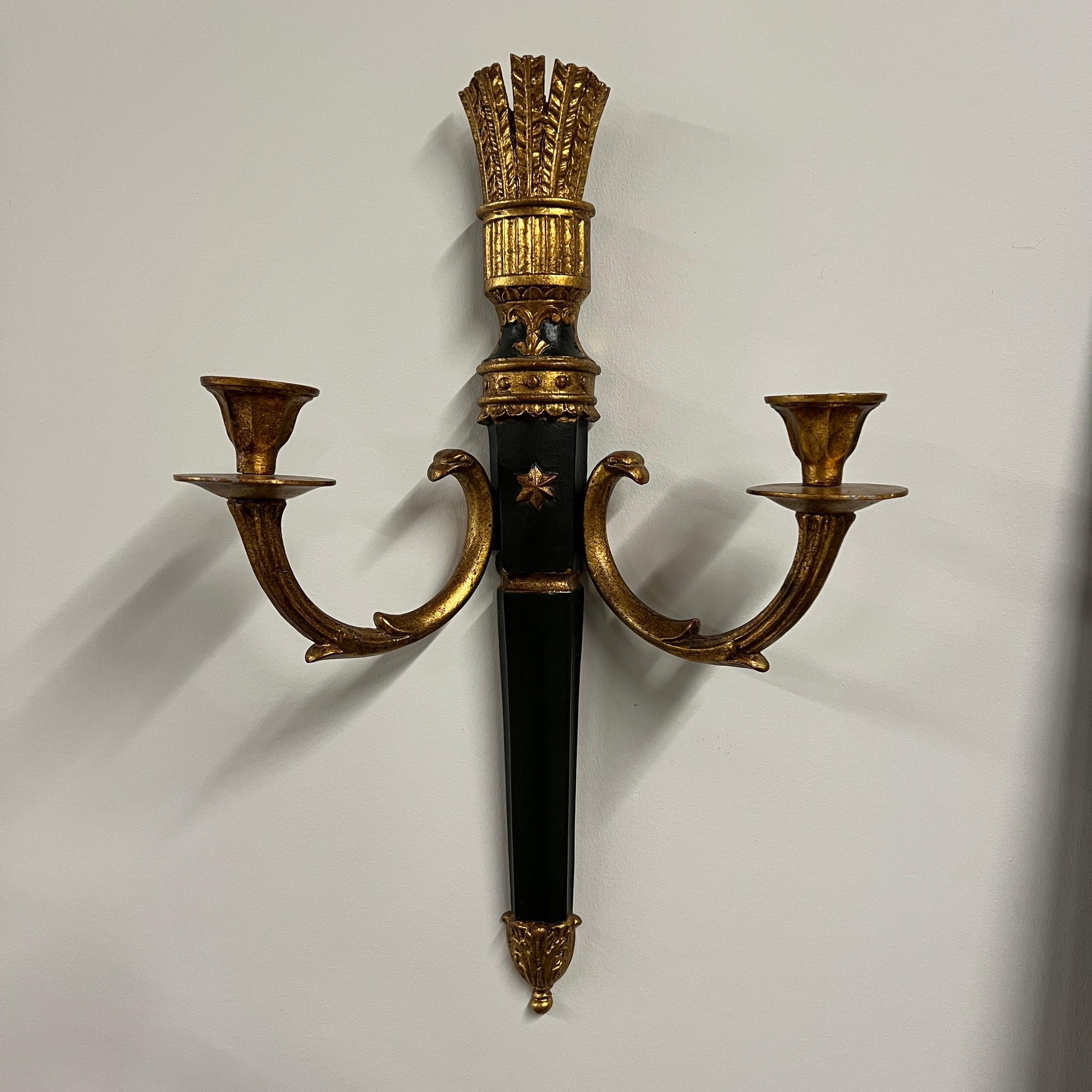 A pair of elegant Italian wall sconces (for use with candles) that feature an ebonized center and parcel-gilt stem supporting two gilt metal candle arms adorned with detail in the style of Louis XVI. Each center body is accented with a raised gold