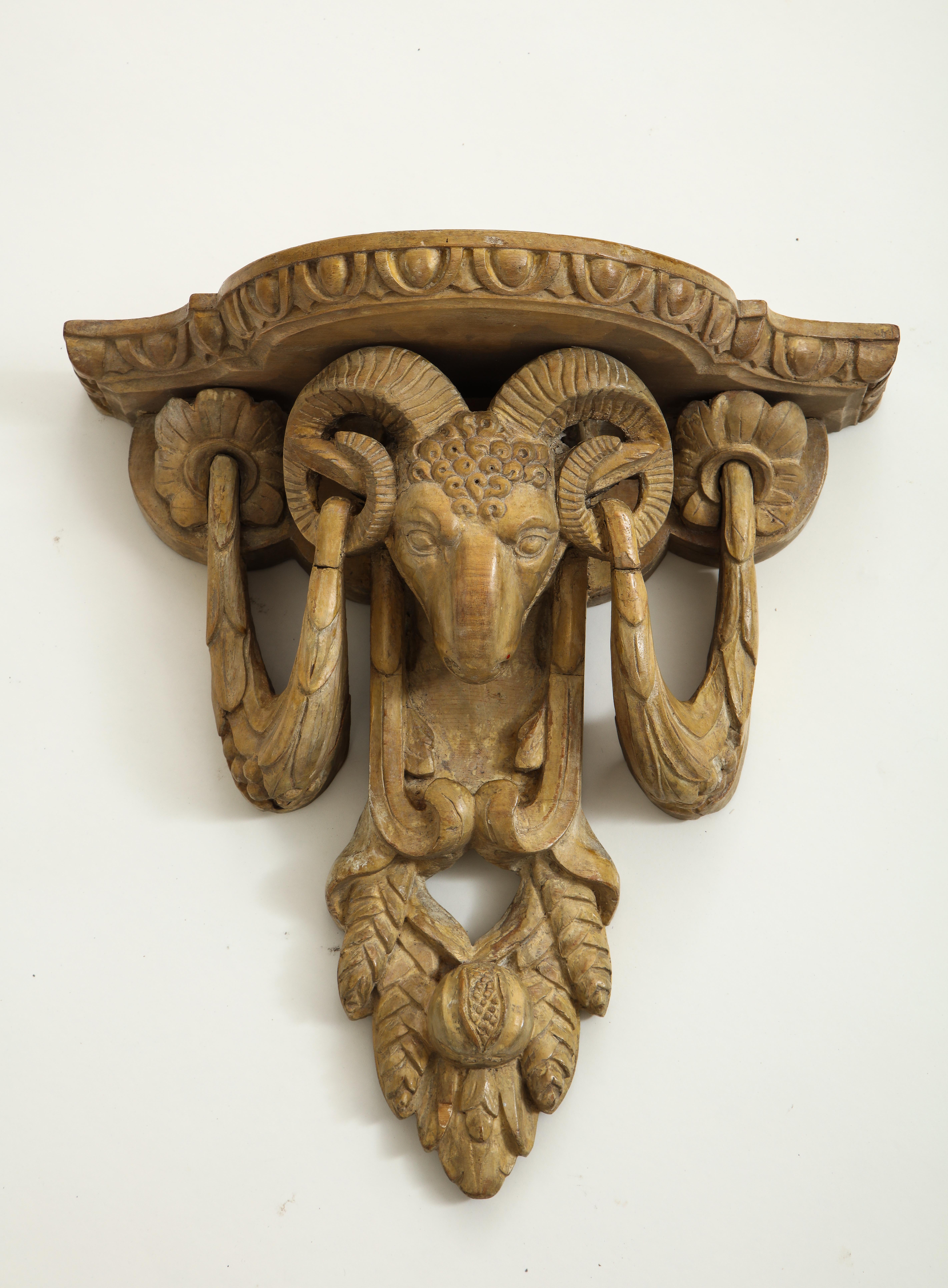 Each with shaped shelved enriched with an egg-and-dart edge over ram's head festooned with garlands with pendant acorns centered by a pomegranate; carved of limed wood.