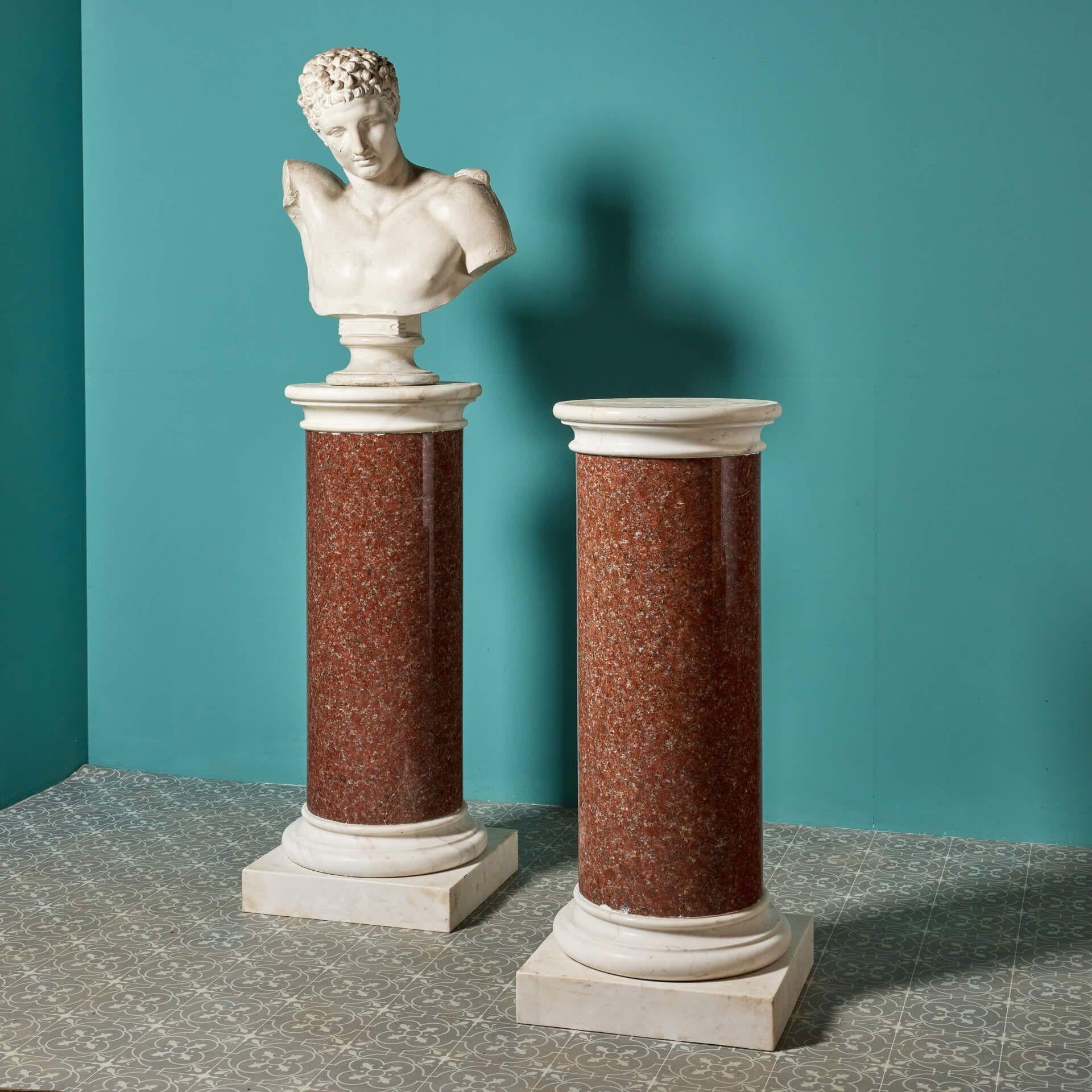 A pair of Neoclassical red granite column pedestals. The 19th century columns' generous size and stature would be fitting inside a grand home or in a garden, perhaps used to show off large scale statues. This impressive pair have a base and socle