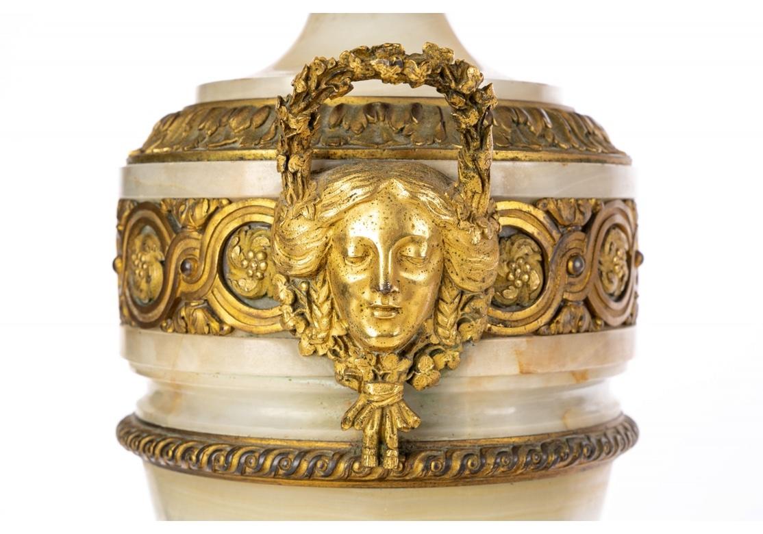 Very fine neoclassical style stone urn form table lamps created from Castelets. The Urns lids and dore foliate decorative bands. The fine wide guilloche neck band with twin female masks supporting the upright wreath form handles. The lower urns with