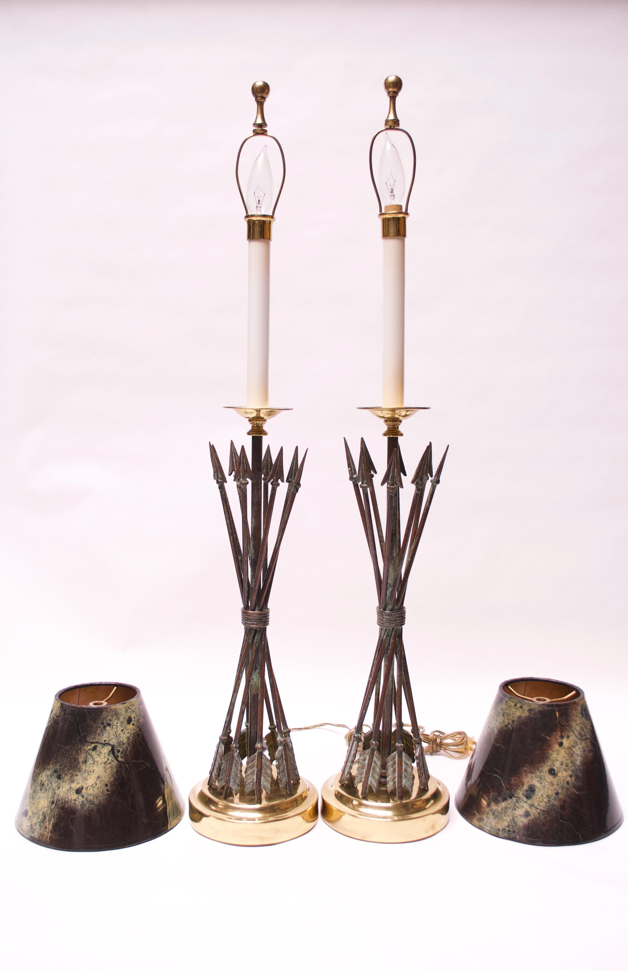 Pair of Maitland Smith tables lamps with crossed arrow motif in a verdigris-bronze finish with brass base, finials, and accents (1980s, Philippines). 
Exceptional, complete examples, retaining their original shades. 
Retains the 