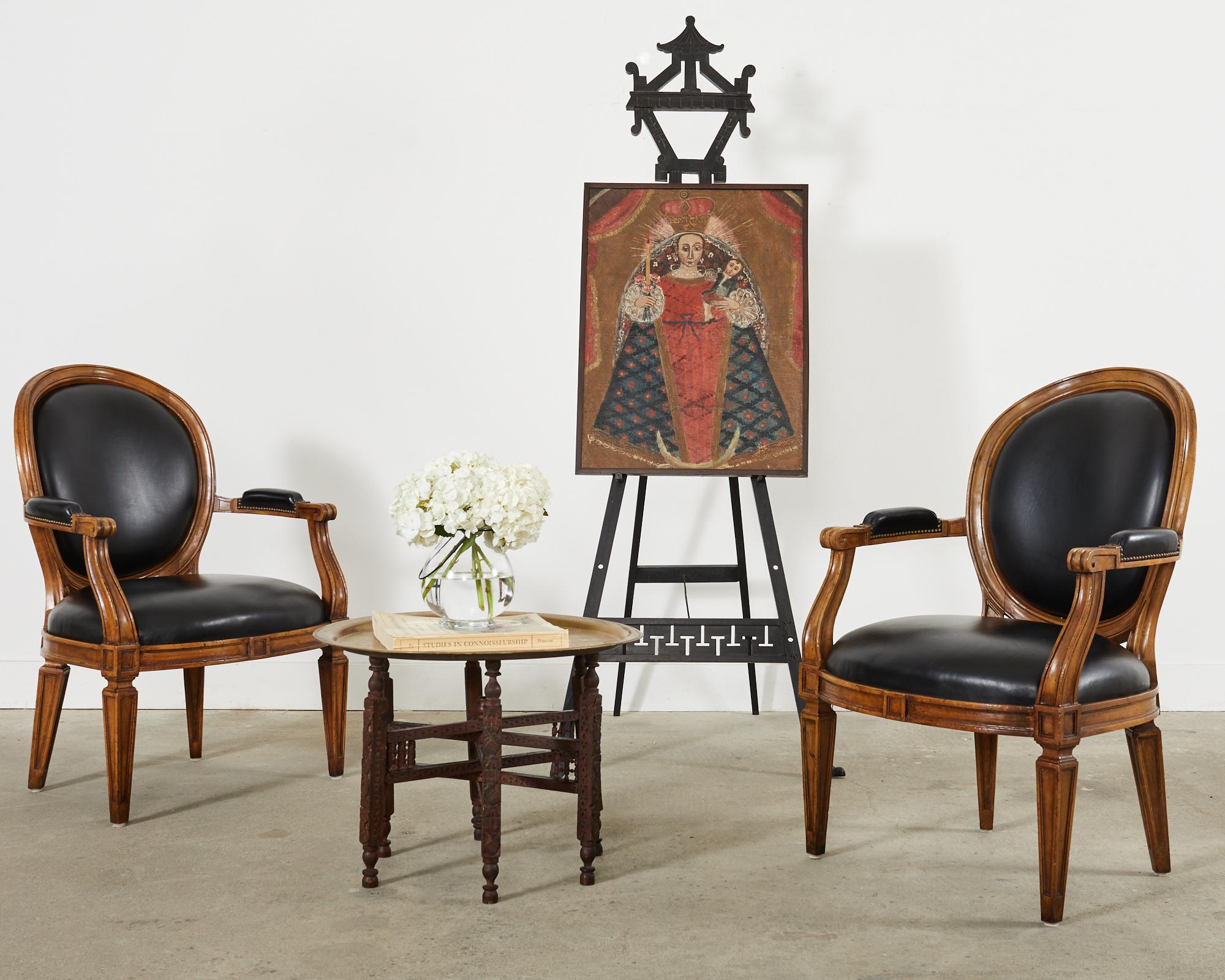 Elegant pair of bespoke carved library armchairs with dramatic black leather upholstery. The large molded frames are made in the neoclassical taste with an intentionally aged, distressed patina on the wood finish to mimic age. Made by Brustlin