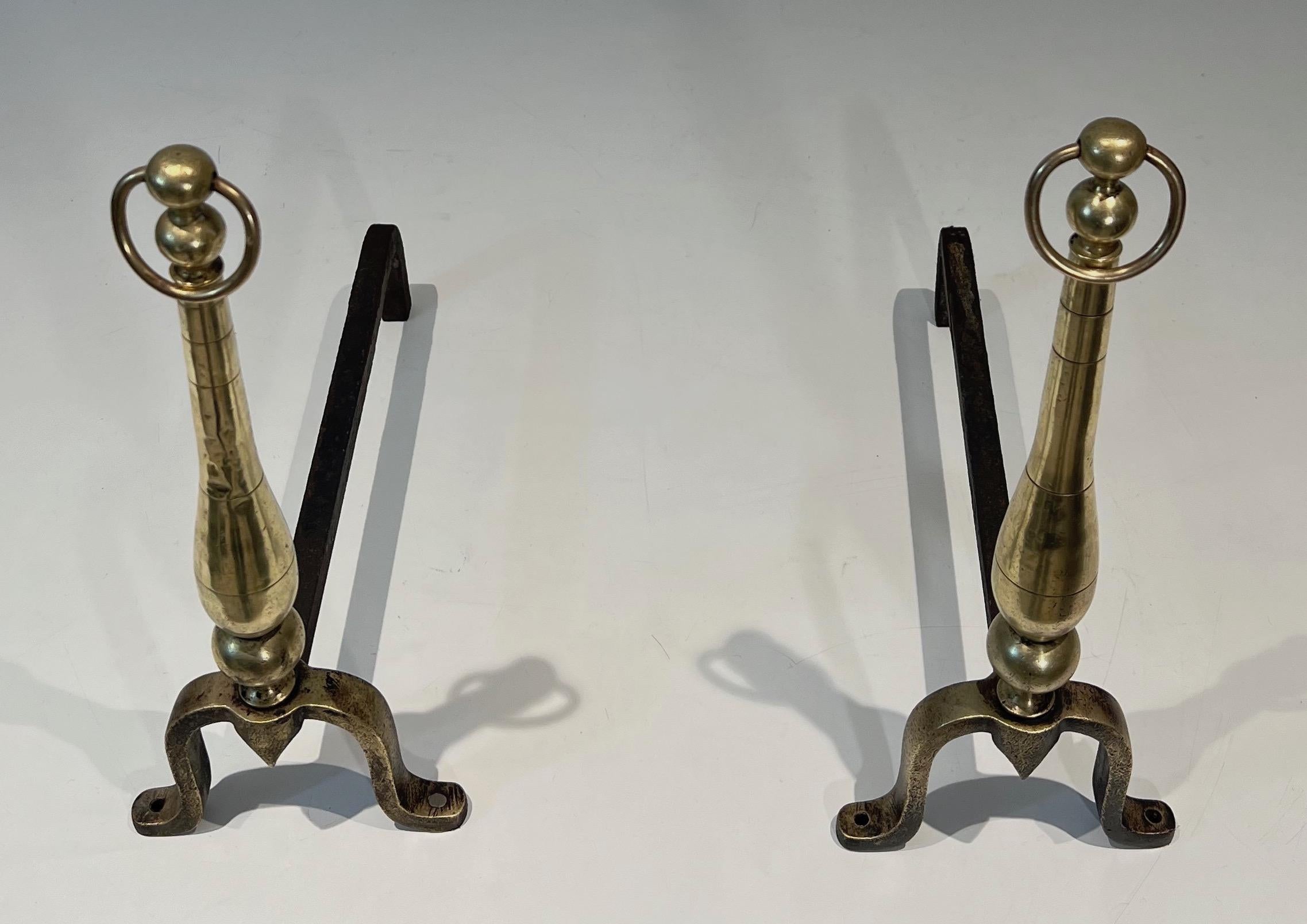 This elegant pair of neoclassical style andirons is made of brass and iron. One of the andirons present small dents on the brass as shown on the pictures. This is a French work. Circa 1970