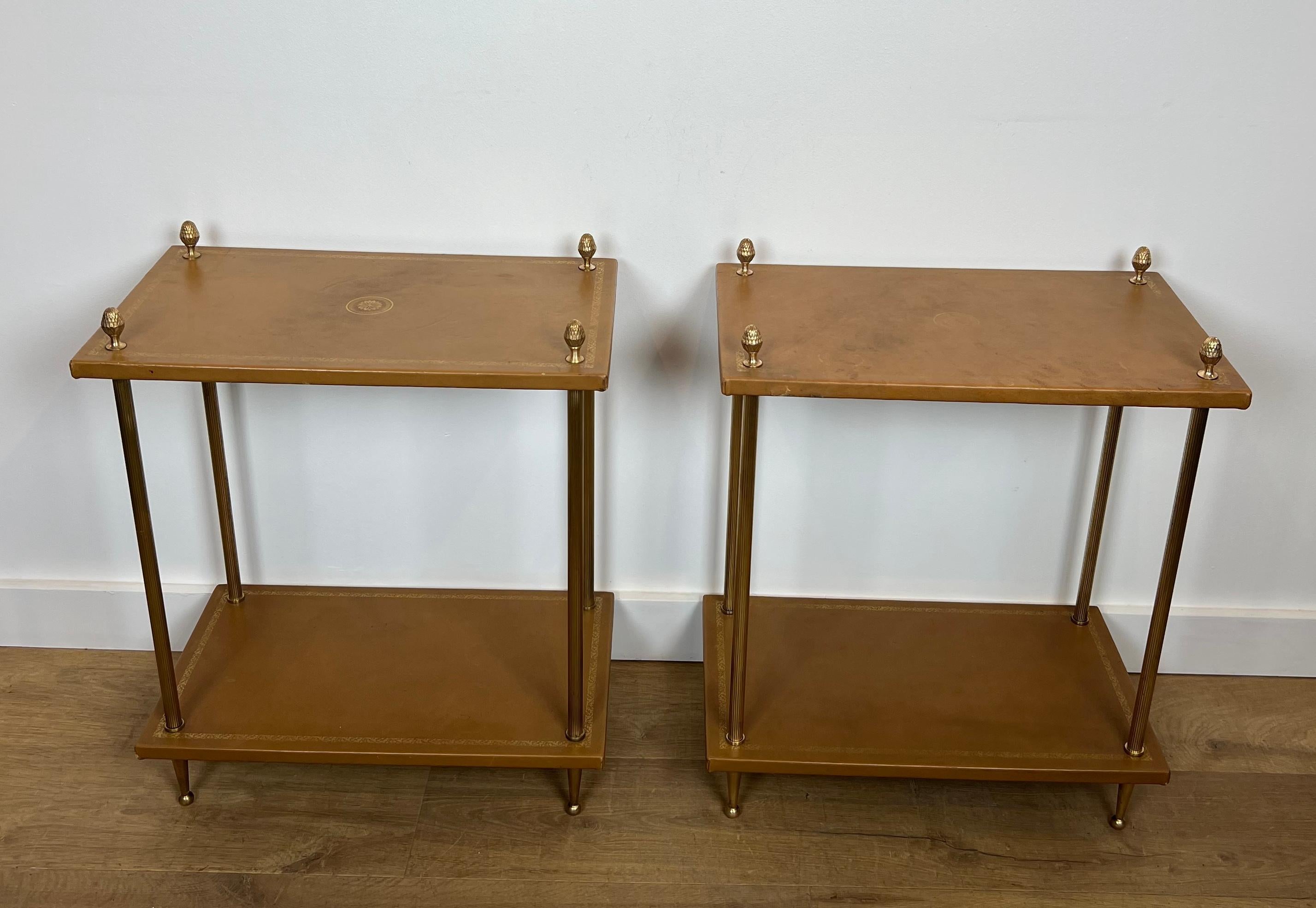This nice and rare pair of neoclassical style side tables is made of brass with fawn leather tops surrounded by a gilt decoration and topped with pine cones finials. This is a French work by Maison Jansen. Circa 1940