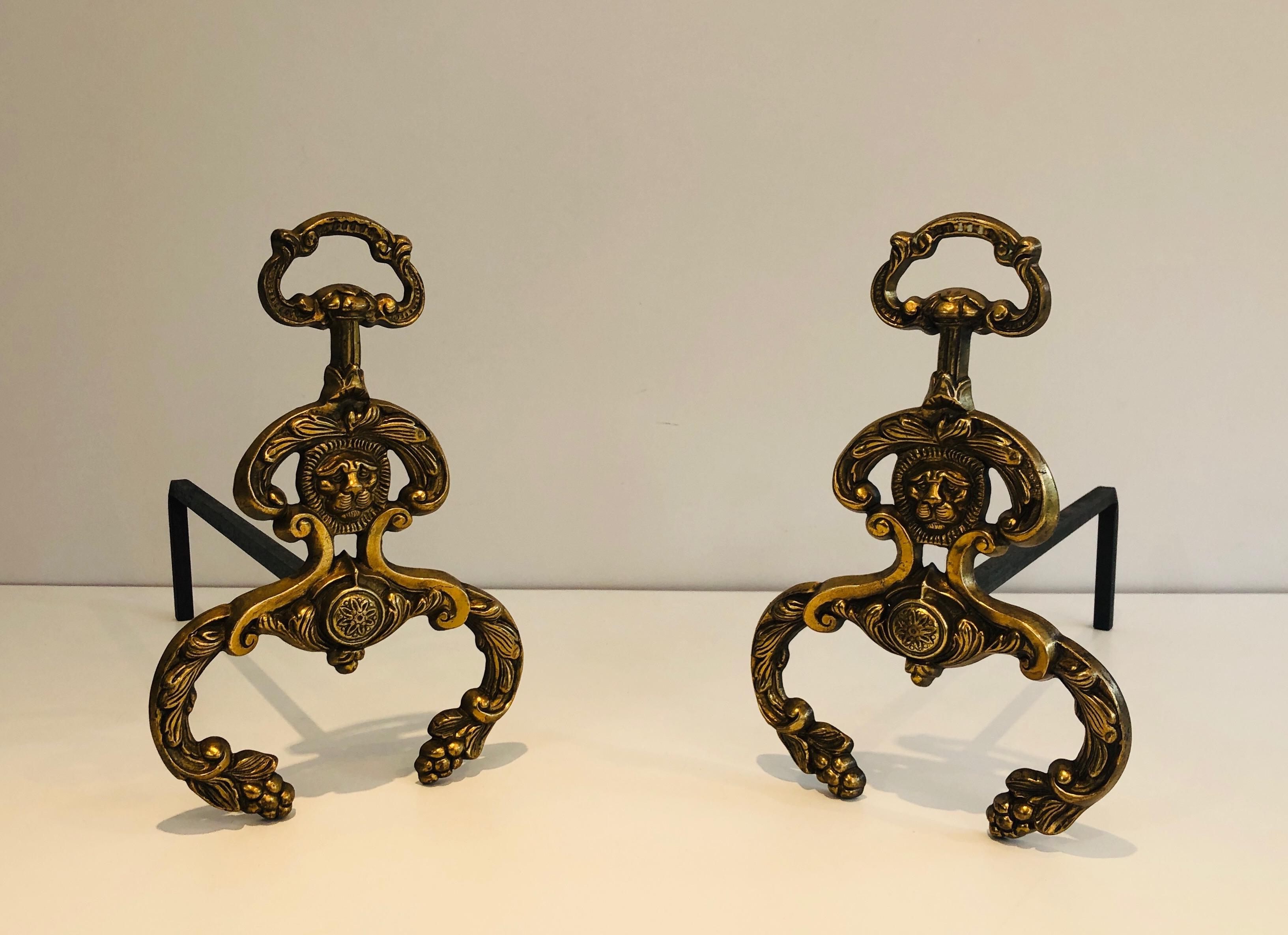 This pair of neoclassical style andirons is made of bronze and wrought iron. These firedogs have lion faces medallions. This is a French work, circa 1940.