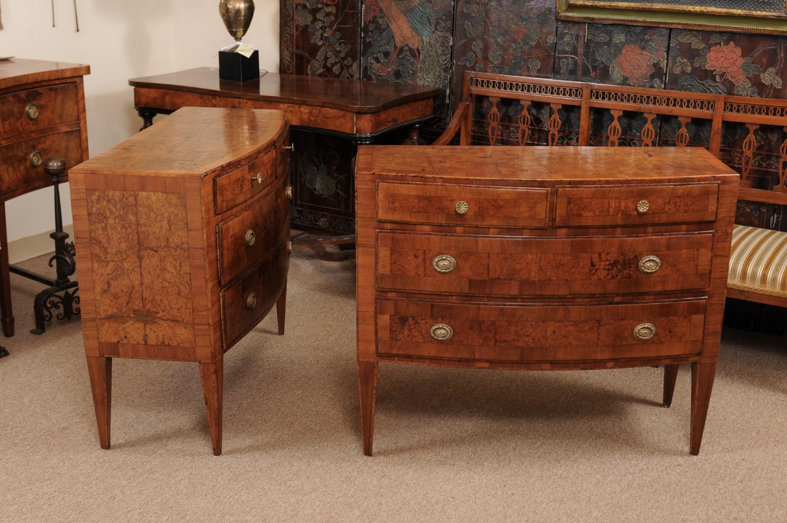 The pair of neoclassical style burled walnut Italian commodes with bow-fronts, 2 small drawers and 2 long drawers below terminating in tapered legs.
