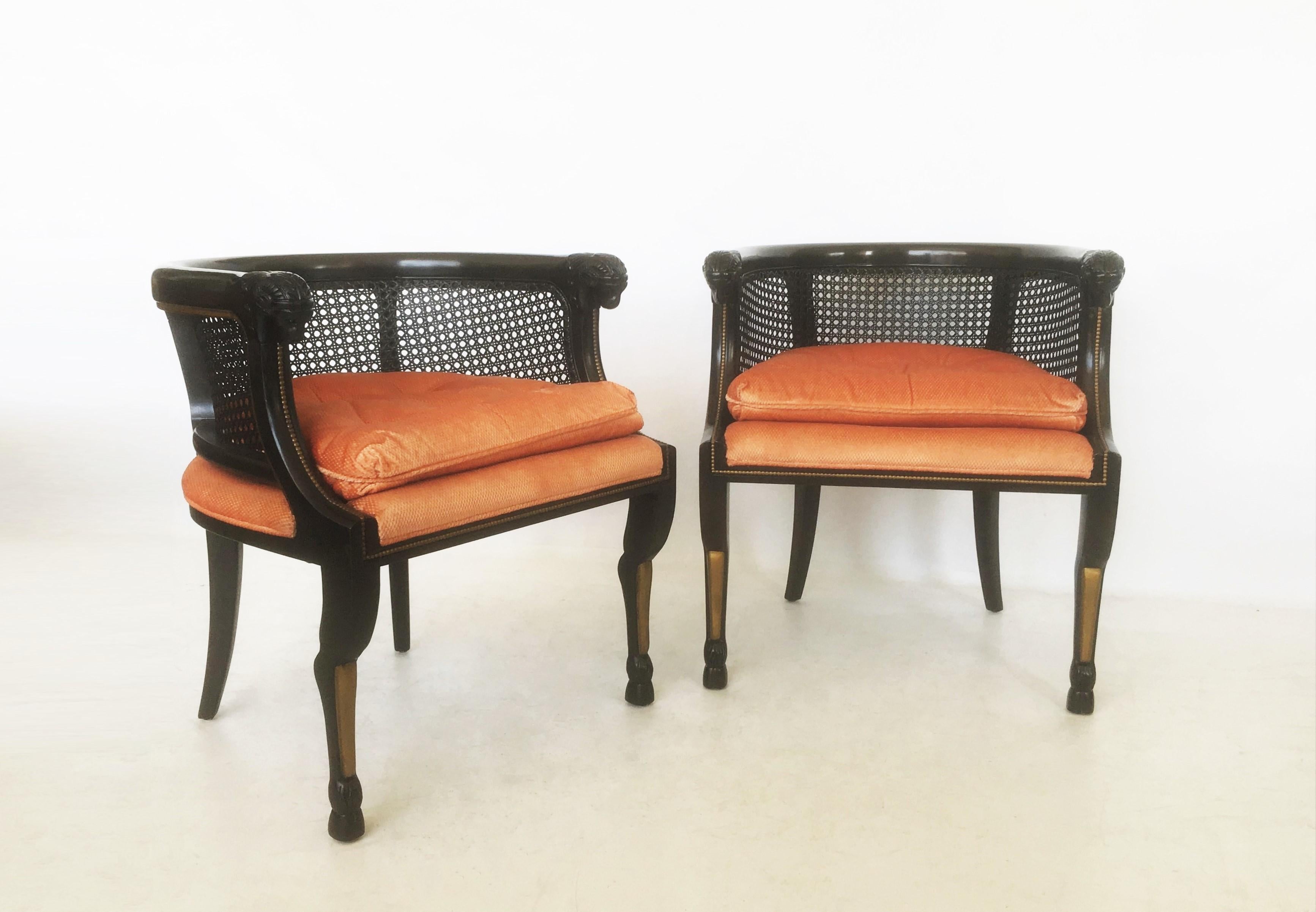Tailored stately pair of ebonized bergères. These armchairs feature a caned barrel back including a rounded edge over a coral colored cushioned seat with finely carved ram's head hand holds. The gentle curve from the back along the arm is very