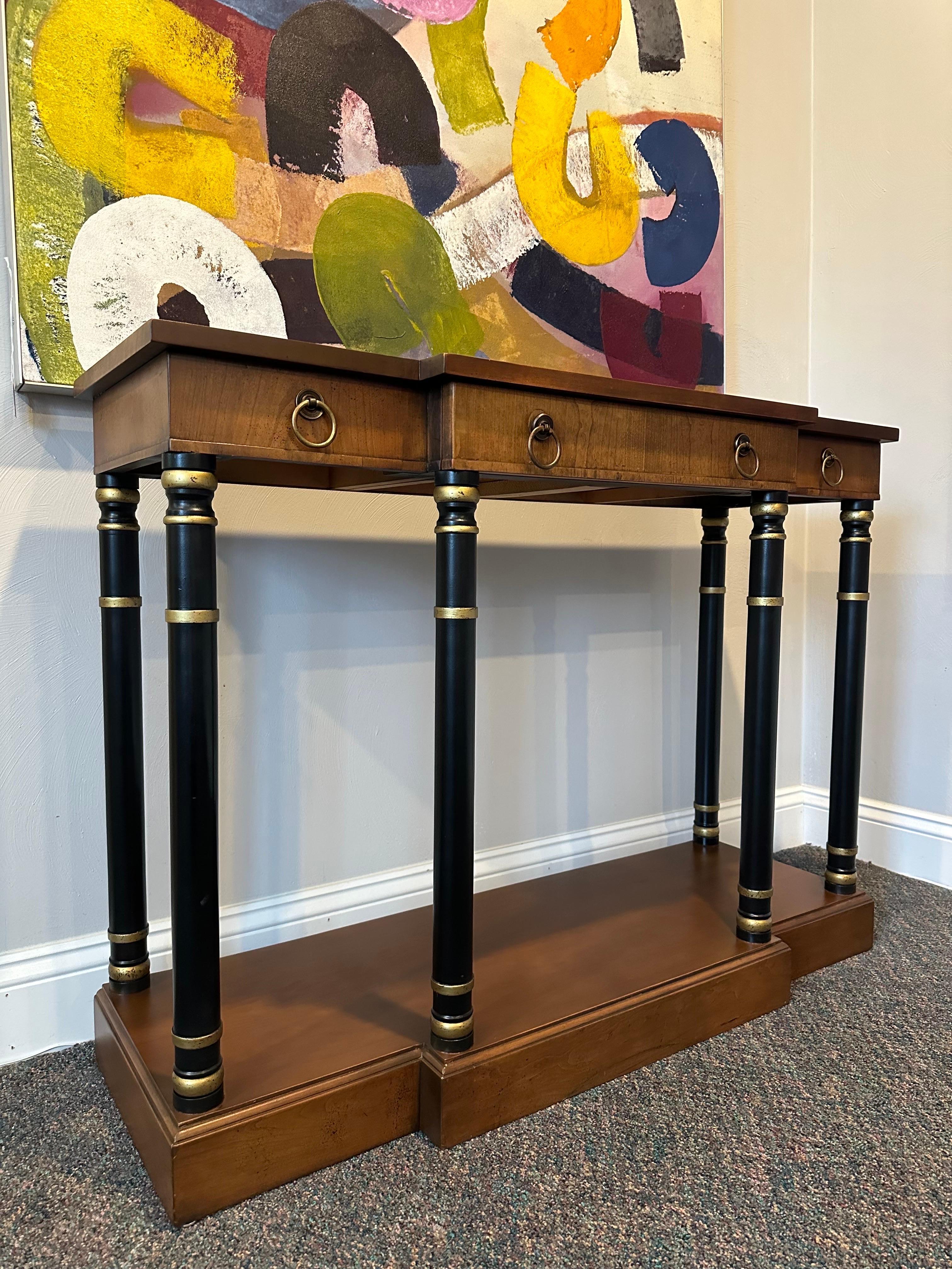 Impressive pair of neoclassical style console table or sideboards. The tables showcase exquisite graining, adorned with decorative brass pulls and complemented by ebonized columned pillars, showcasing impressive craftsmanship and attention to