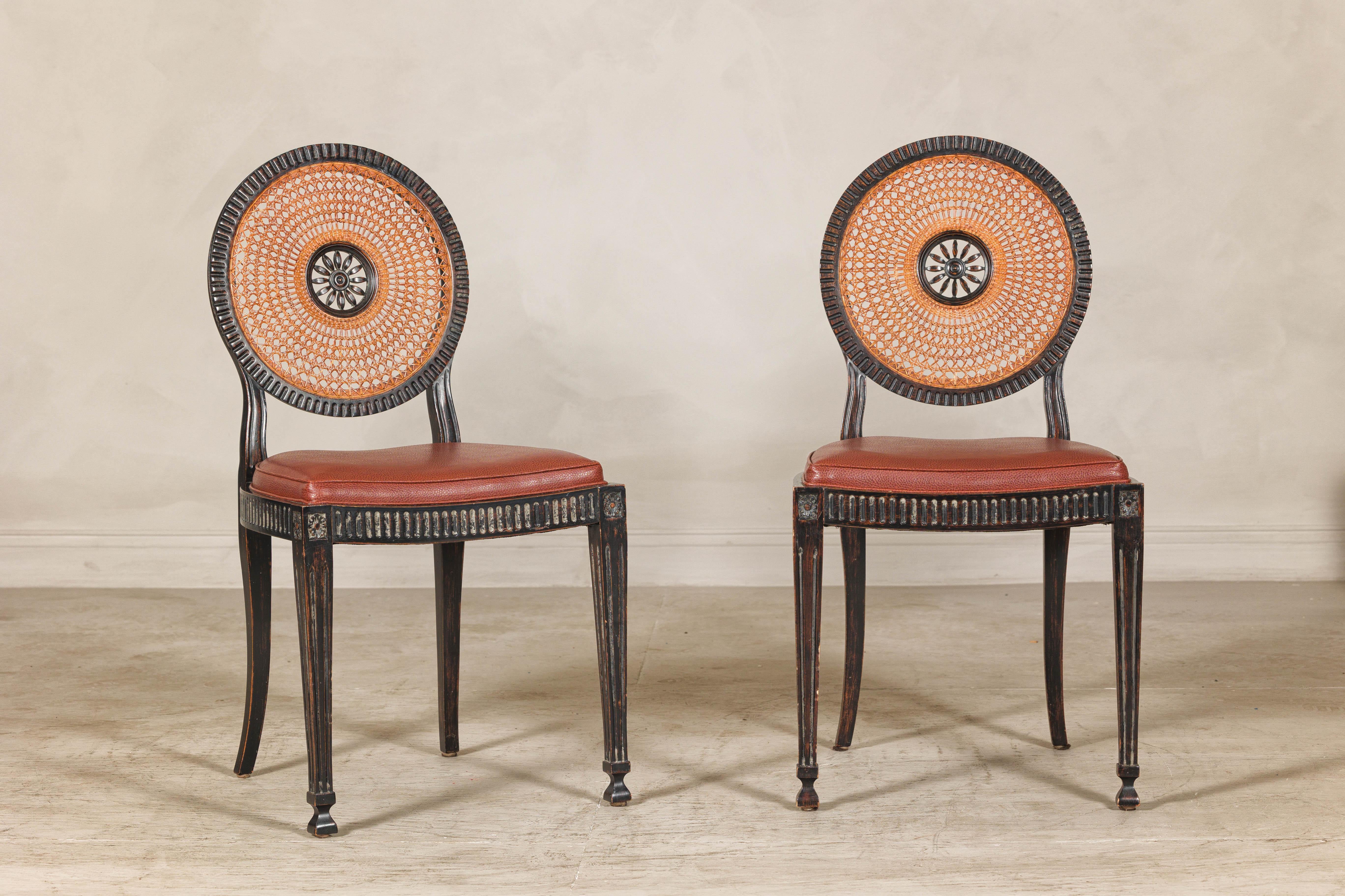 A pair of Anglo-Indian Adam style hardwood dining chairs with rattan backs. Elevate your interiors with this exquisite pair of chairs, dating from the 1930s–1950s and inspired by Neoclassical Adam-style and Anglo-Indian design influences. Crafted