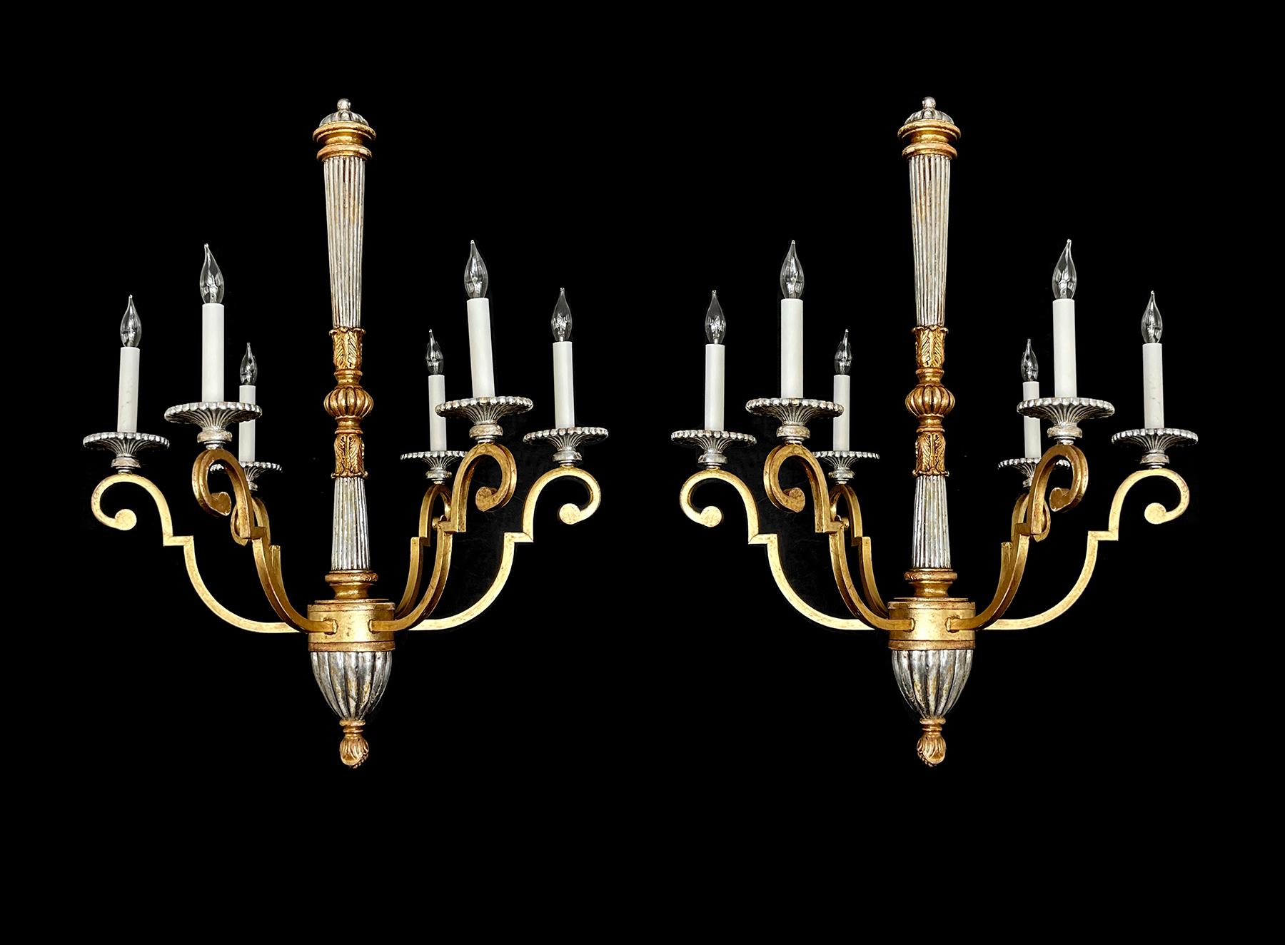an elegant pair of chandeliers in the neoclassical taste decorated in a silver and gold leaf finish; the reeded central support joined at the mid-section with a gadrooned sphere and acanthus leaf collars all above a tapering reeded base ending in a