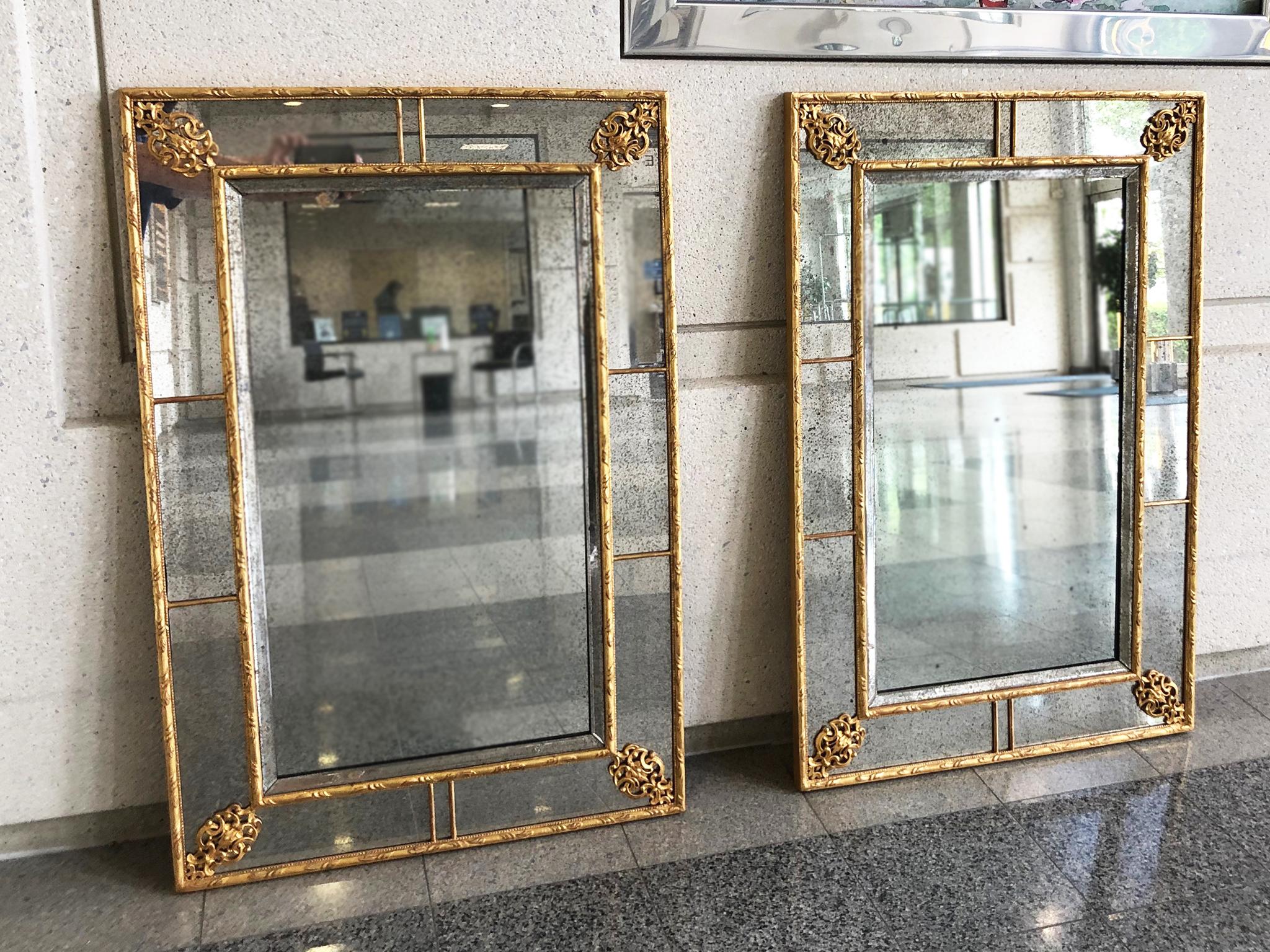 A pair of vintage wall mirrors, crafted in the 20th century. They are designed in the neoclassical style and comprised of antiqued glass that has been paneled and beautifully trimmed in giltwood. The mirrors are also backed with a protective sheet