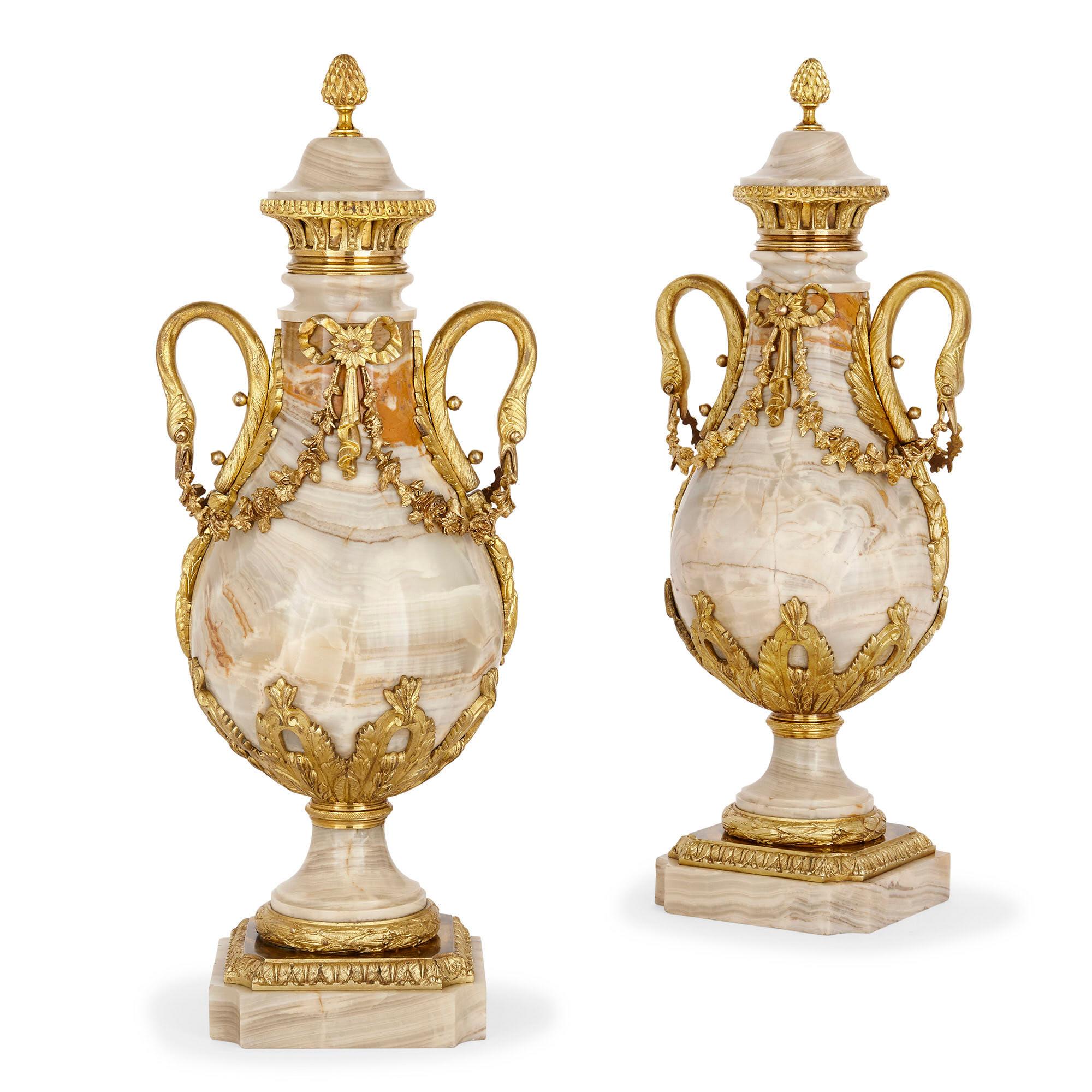 Each vase in this pair, crafted from gilt bronze mounted onyx, is baluster shaped in a manner characteristic of the grand and elegant neoclassical style. Supported by a square onyx base, each vase stands on a curvilinear gilt bronze mounted onyx