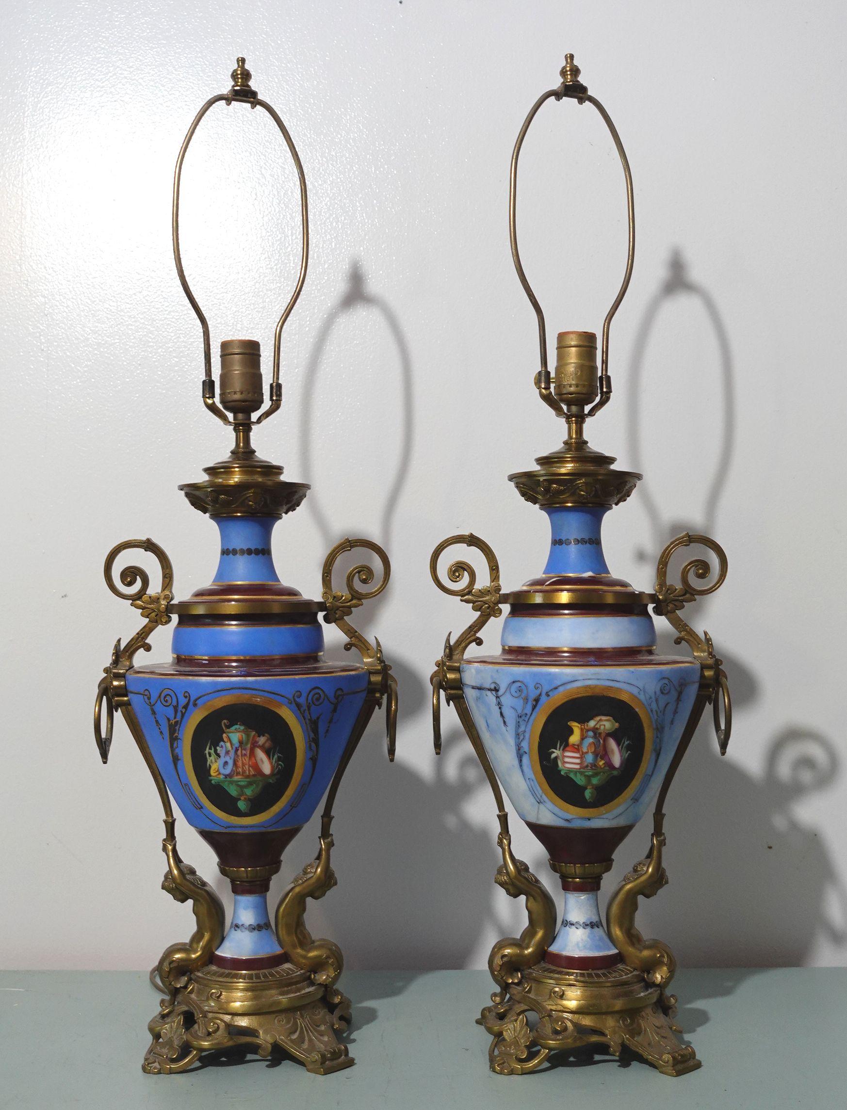 Paire de lampes en porcelaine de style néoclassique, à fond bleu mat. Bases de piedouche brunes et bleues et bord intérieur du col. Sur le corps, le décor du médaillon central sur deux faces représente un caractère polychrome de style antique. Des