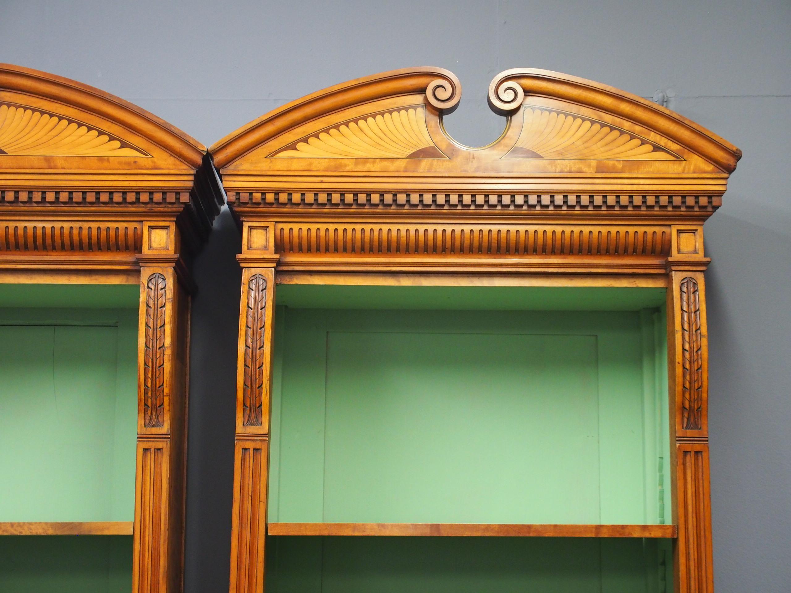 With restorations, pair of neoclassical style, tall satinwood open bookcases, circa 1880. Surmounted by a scrolled, broken pediment with satinwood, boxwood and ebony inlay over a moulded, fluted dentil cornice. This is flanked by carved and fluted