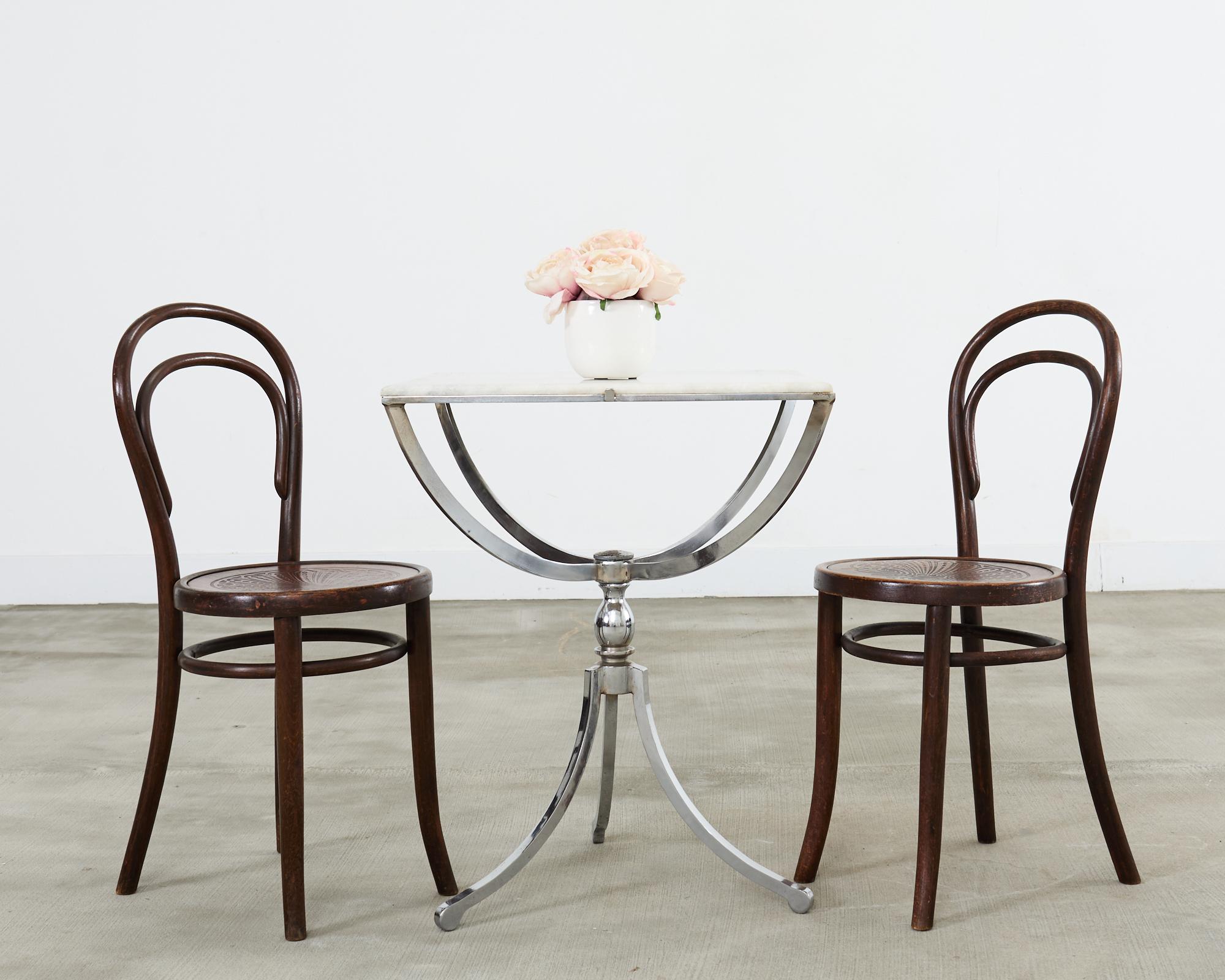 Opulent pair of rare French chromed steel bistro tables featuring granite stone tops. The early 20th century tables are constructed from thick bar steel frames with an aged chrome finish. The granite squares are supported by four gracefully curved