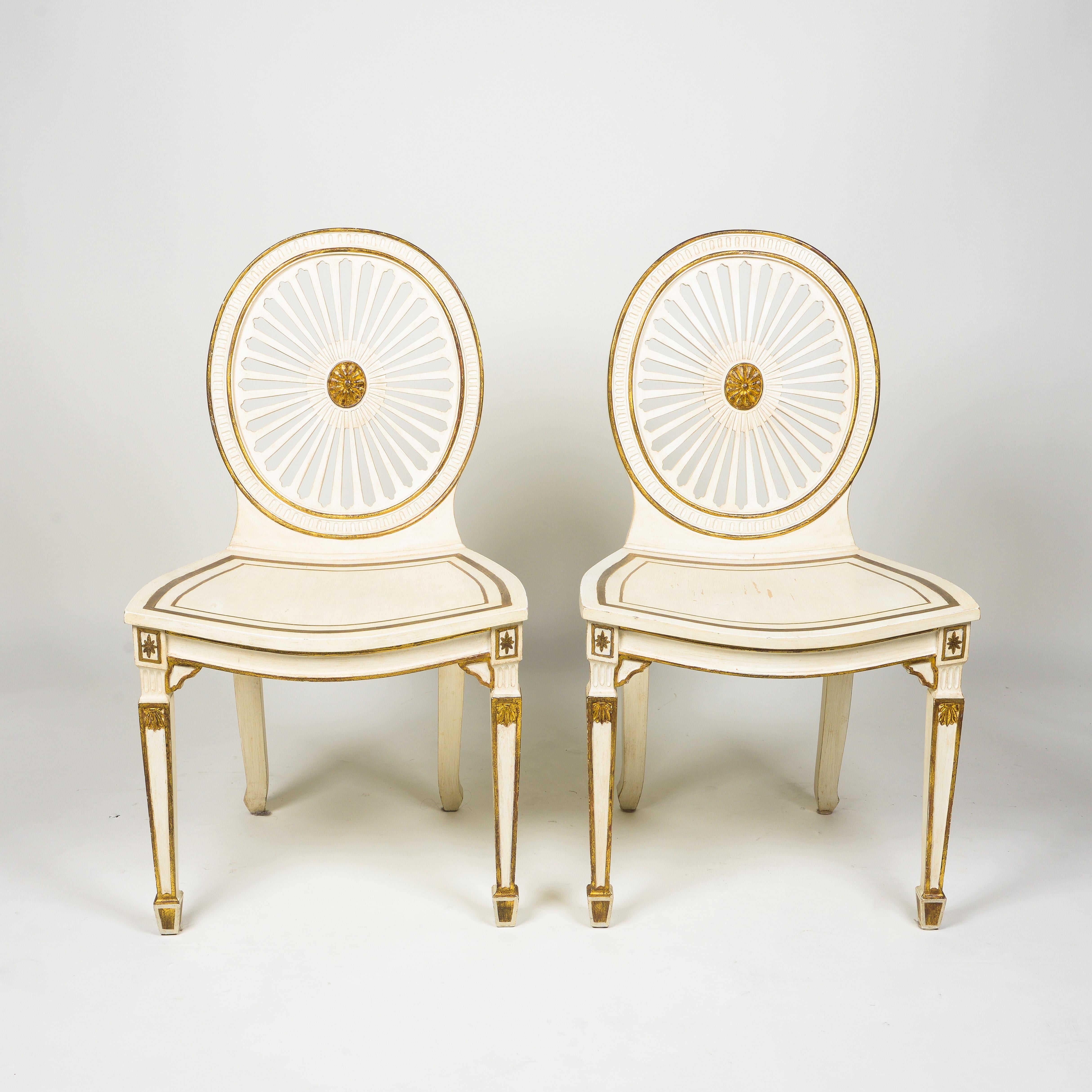 Each with an oval back in the form of a pierced fan paterae centered by a gilt floral roundel and edged in gilt; the dished seat with gilt banding raised on front square tapering legs headed by stop-fluting and painted floral roundels and