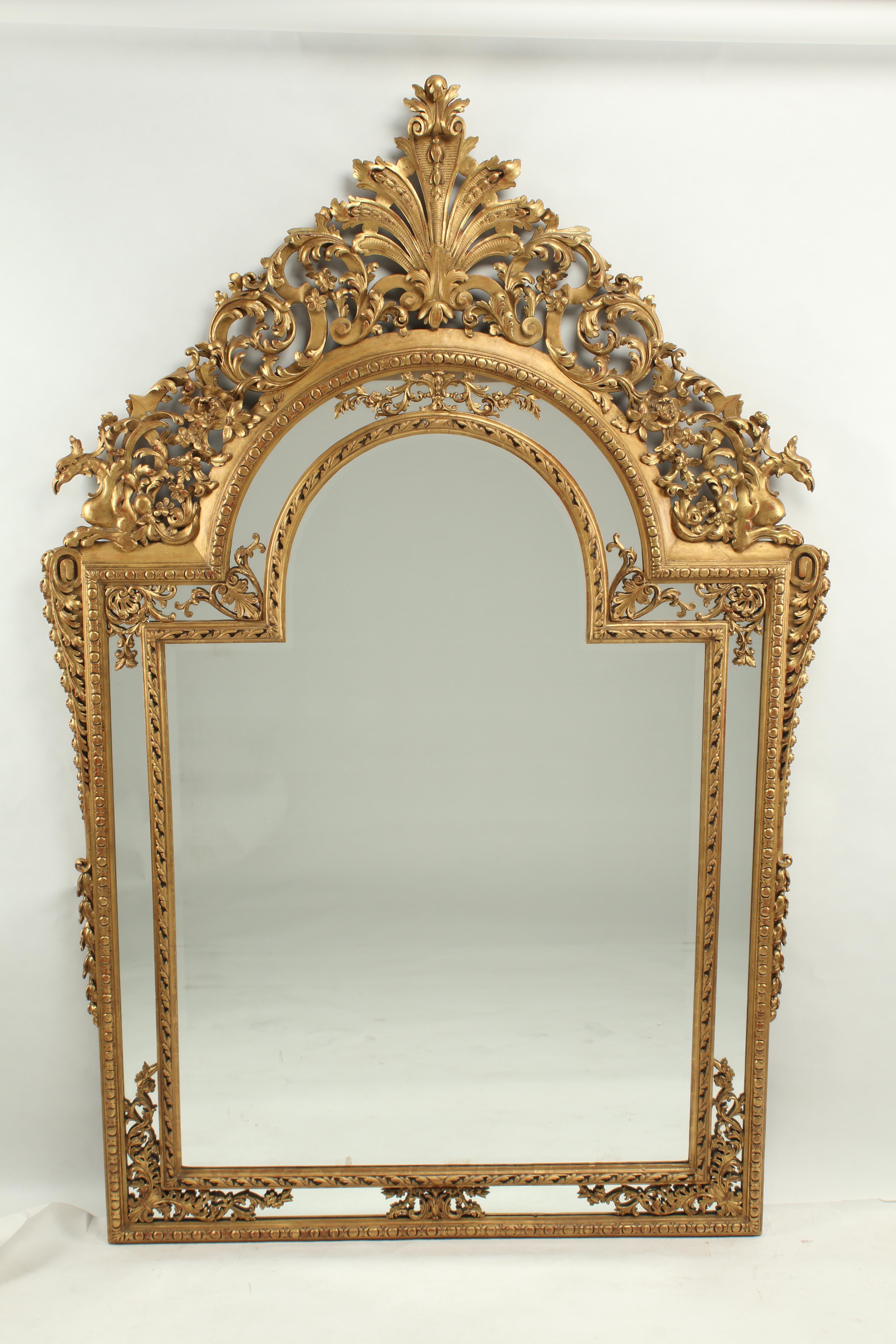 Questa eccezionale coppia di specchi in legno intagliato e dorato in stile neoclassico presenta un design elaborato e ricco di dettagli. Lo stemma presenta un importante motivo a palmetta affiancato da intricate volute aperte, foglie d'acanto e