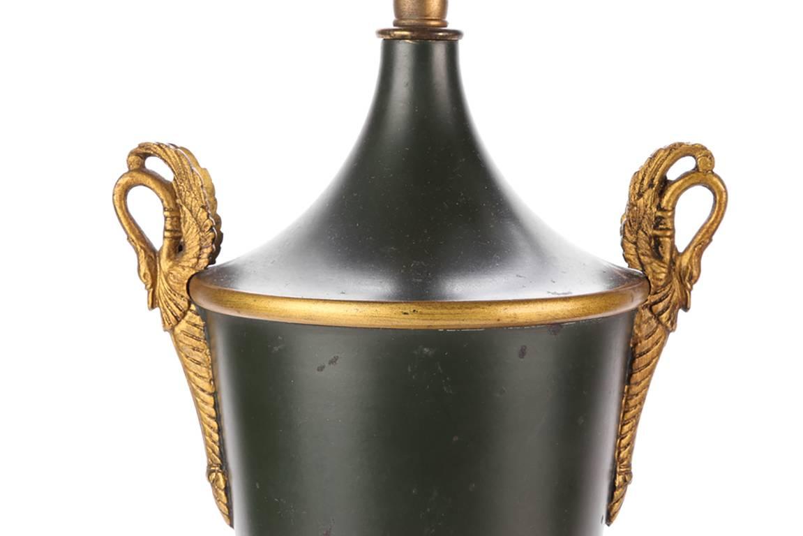 Pair of neoclassical tole urn form lamps, twin-light dark green tole urns with twin brass swan form handles and gilt palmette decoration, raised on tiered pedestal bases with gilt palmettes, adjustable top bars for shades.

Condition: Expected