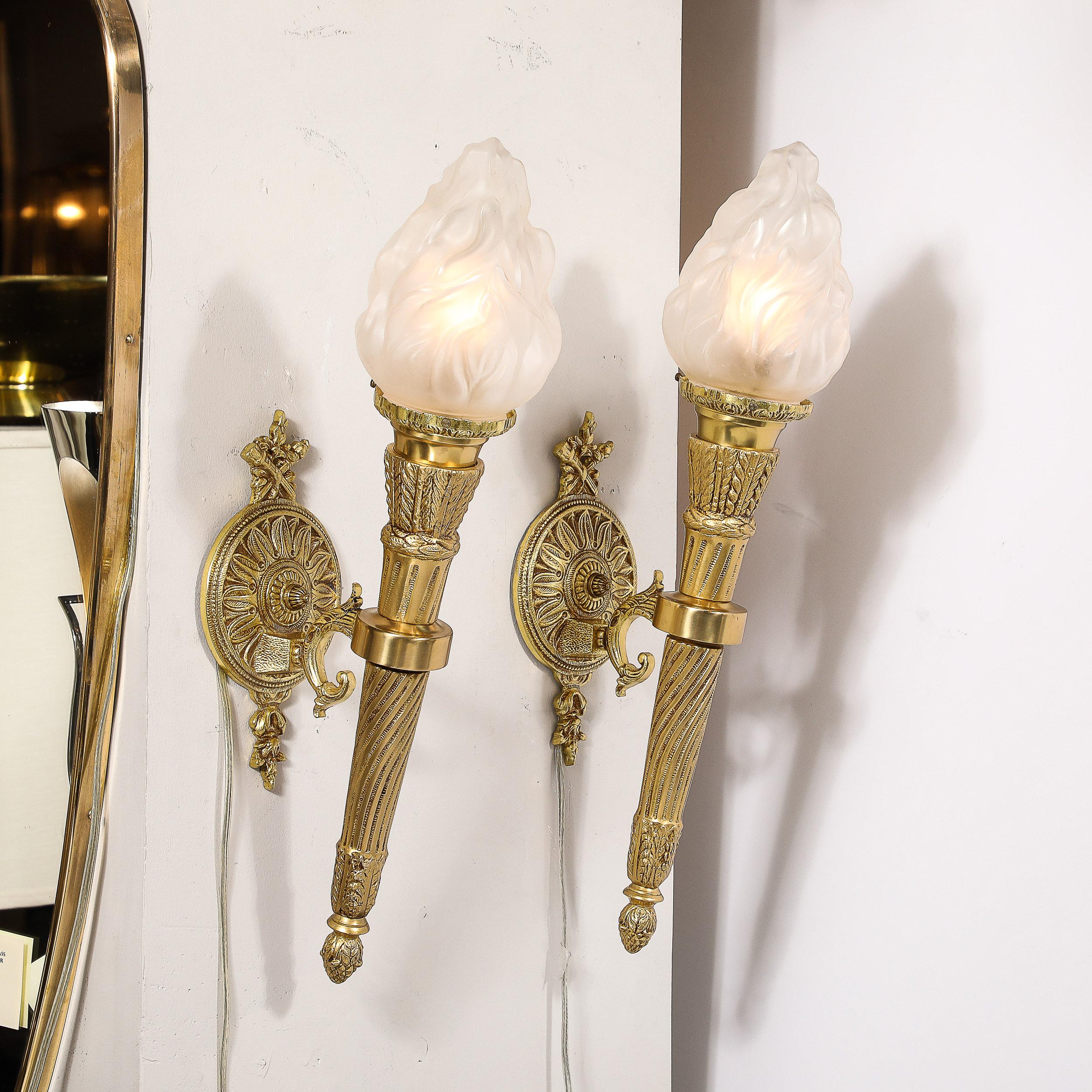 This regal and ornate Pair of Neoclassical Torch Sconces in Frosted Glass and antique  brass originates from France during the latter half of the 20th Century. Featuring frosted glass shades reminiscent of torch flames, supported by a handle like