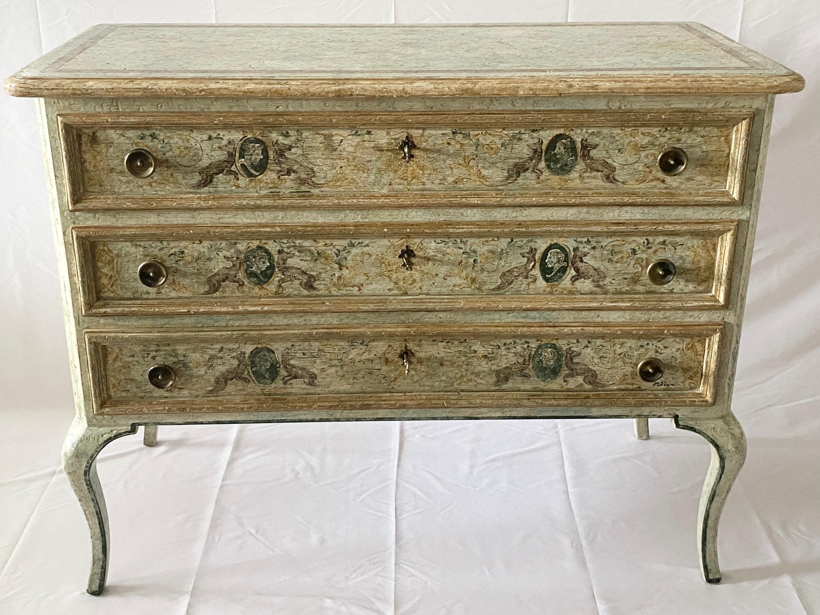 A fine pair of Neoclassical Style Commodes or Venetian Hand Painted Chest of Drawers featuring fine scroll work in hues of yellow ochres, olive greens and blues on an antiqued white background. The overall warm tones of the paintwork are accentuated