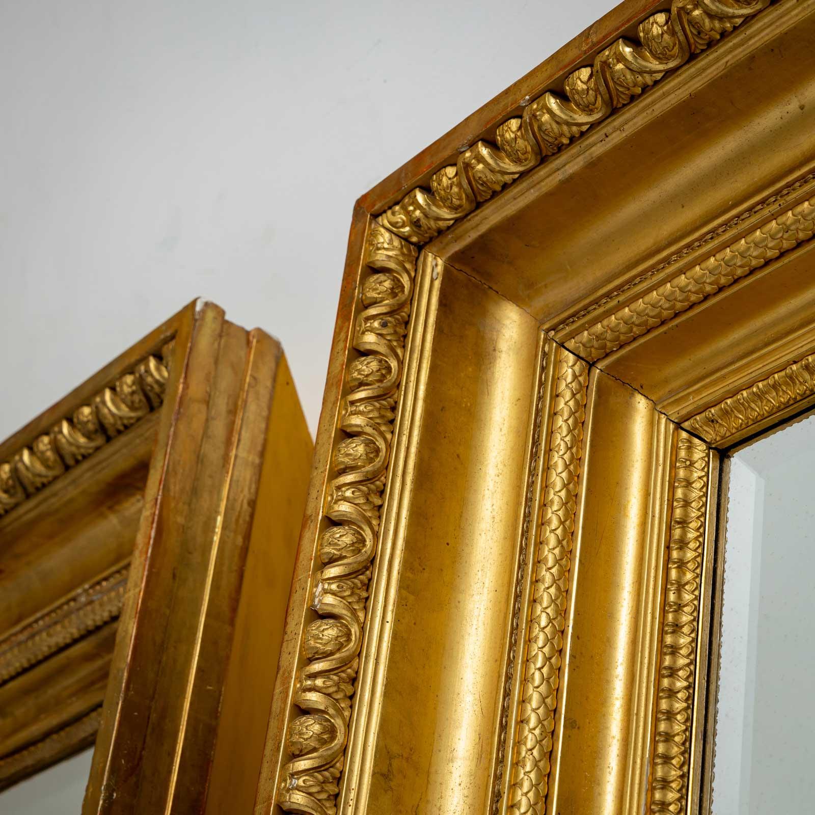 Paire de grands miroirs muraux dans un cadre en stuc patiné or avec une moulure fortement profilée. Une frise de feuilles forme le cadre extérieur. Très belle dorure d'origine, le bolus rouge ne transparaissant que par endroits. 