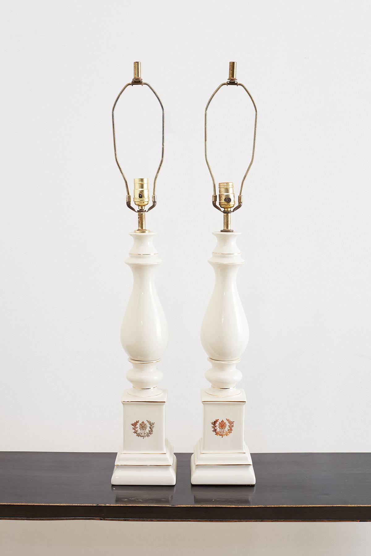 Gorgeous pair of white porcelain table lamps having a baluster form mounted on square pedestals. Made in the neoclassical taste with a parcel gilt finish featuring a laurel wreath crest on the fronts. Topped with original brass hardware, harps, and