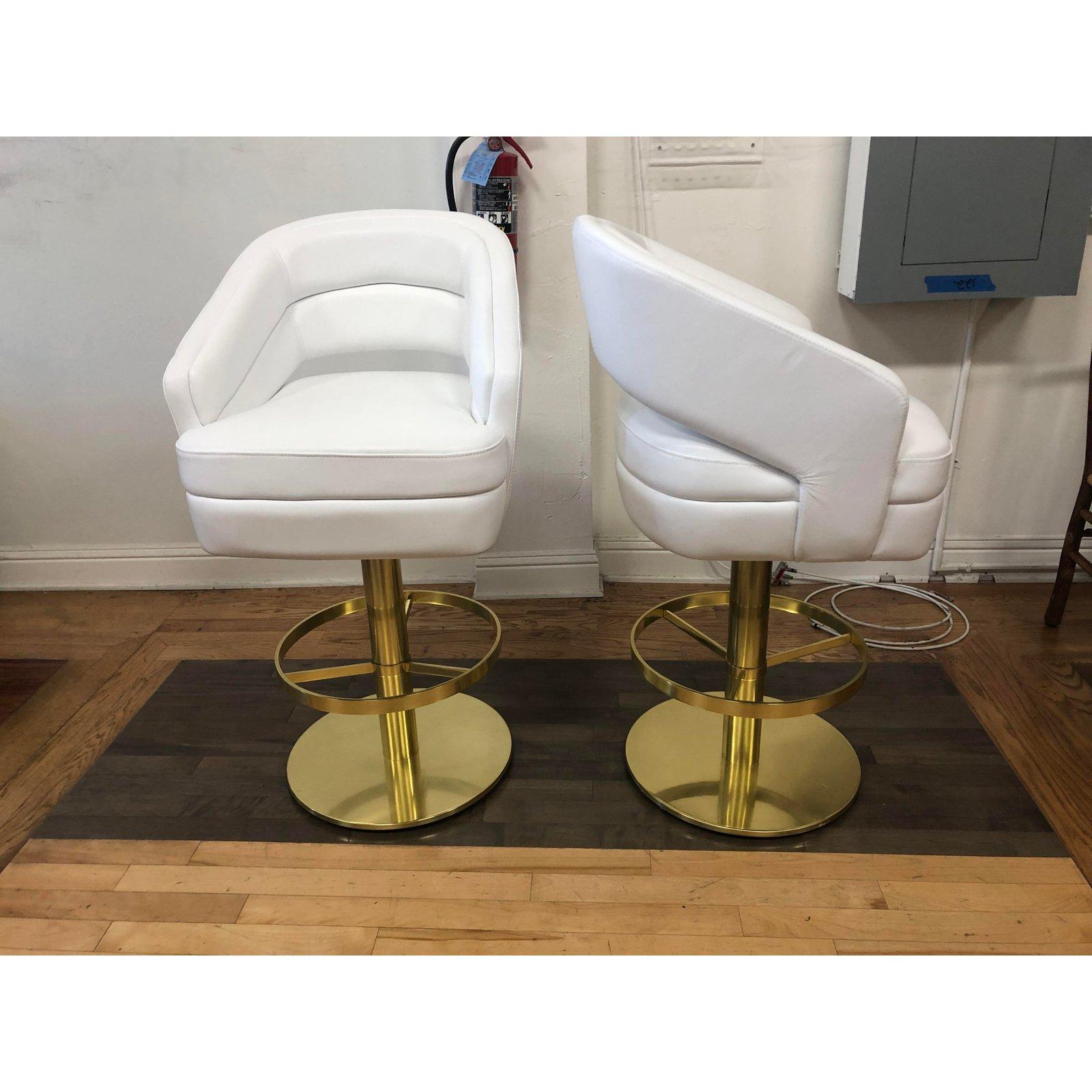 Russel barstool by Essential Homes. A modern nod to an inspiration of Hollywood Regency and Art Deco. Upholstered in a white leather with a golden polished brass base. The base can spin 360 degrees, providing stress-free movement to delve into the