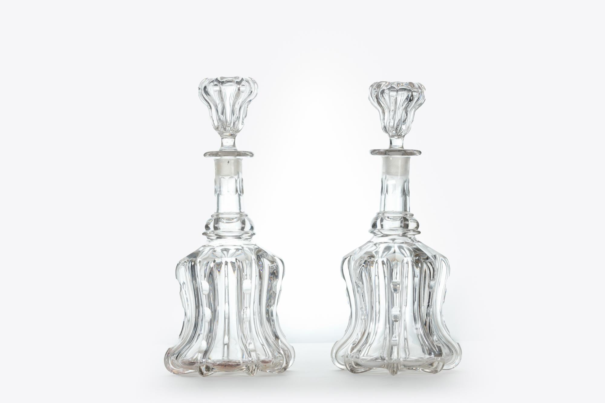 Pair of bell-shaped glass decanters decorated with moulded vertical pillars below broad shoulder rings. The stoppers are of inverted bell form also featuring moulded pillars to match the decanters. This shape is commonly known as “Newcastle