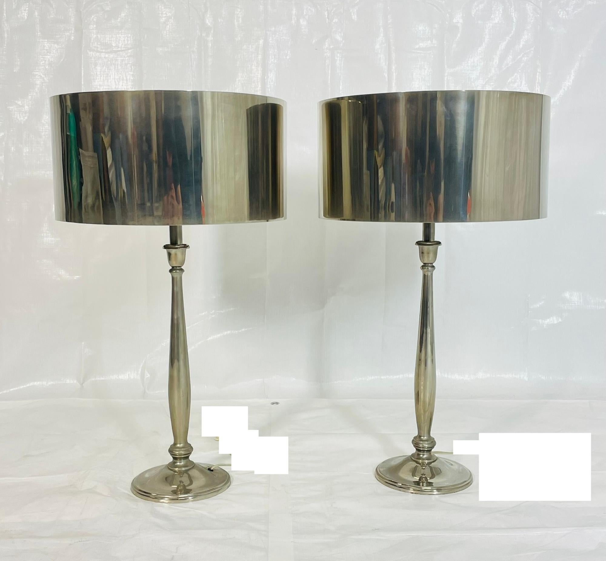 A sleek and elegant pair of nickel-plated table lamps featuring tall, tapered columns and coordinating nickel-finished round drum shades. The reflective metal shades create a bold, sculptural profile and deliver a sophisticated modern look ideal for