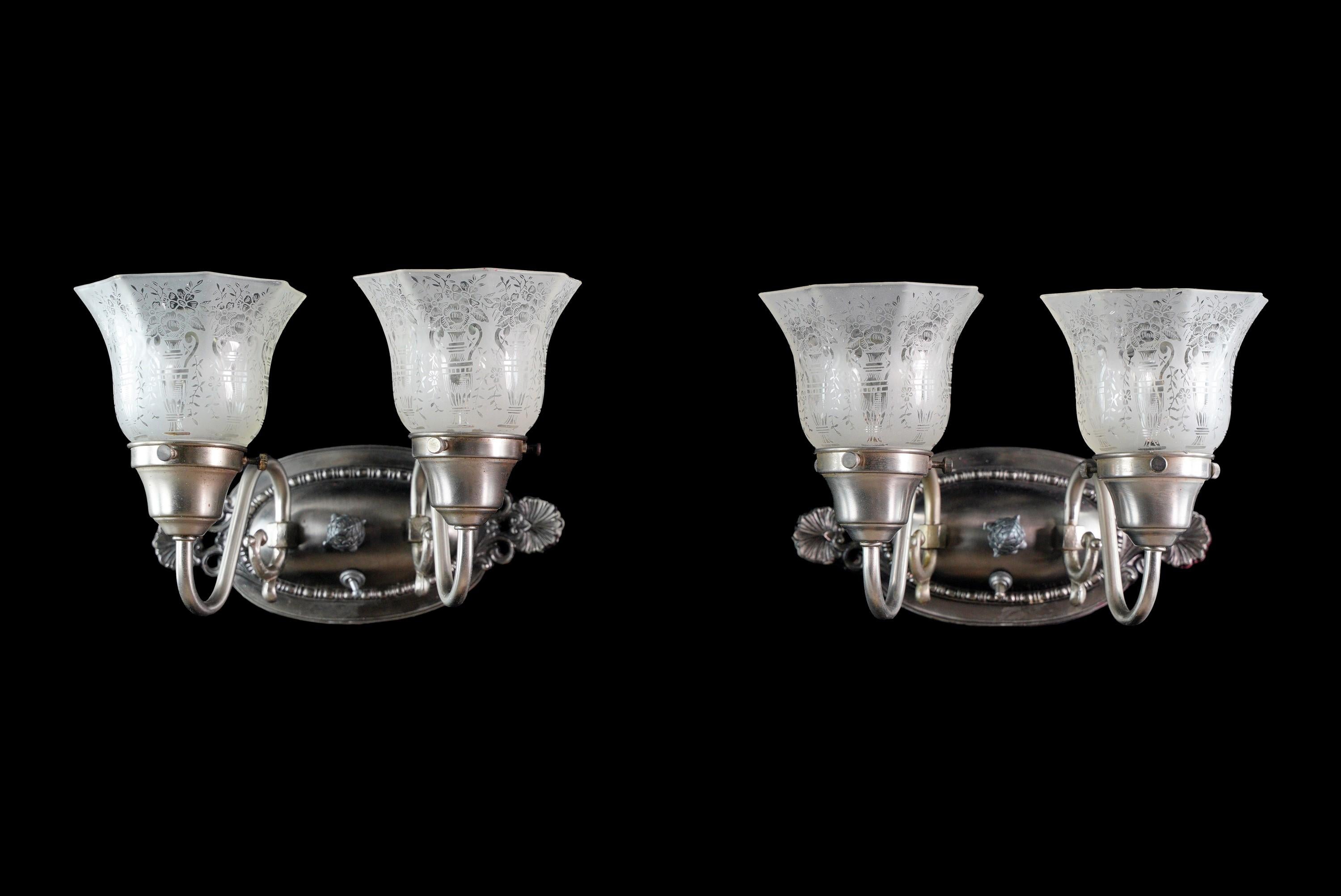 Nickel plated two arm wall sconces with frosted and etched glass shades with urn and floral detail. Cleaned and restored. They are in good condition, with some rust. Priced as a pair. The price includes restoration of cleaning and rewiring. Please