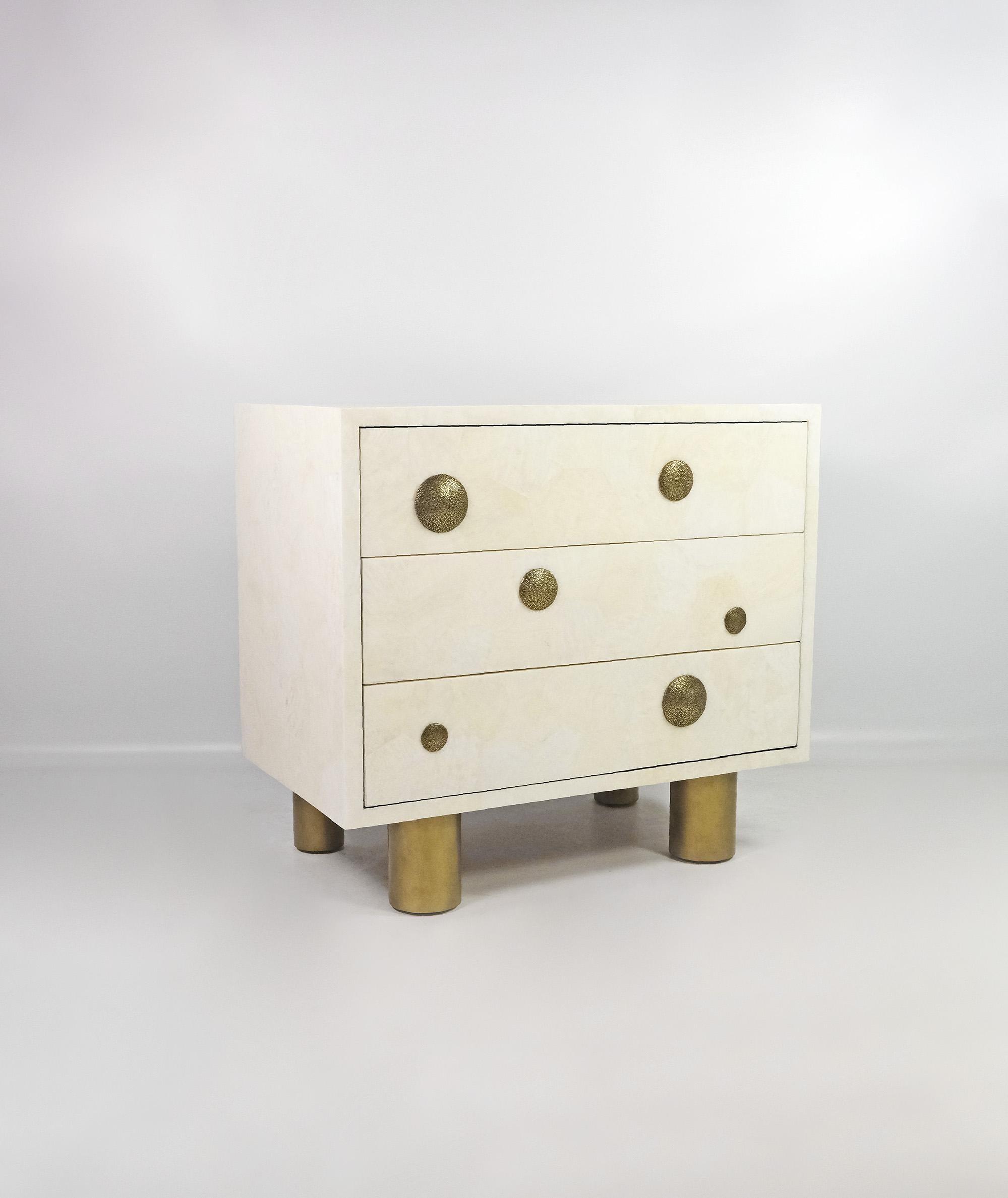 The bedside table is made of white rock crystal marquetry with a polished satin finish.
It has 3 drawers on push to open rails, with casted bronze decors. 
The nightstands seats on four cylinder legs finished with an antic brass patina.

The