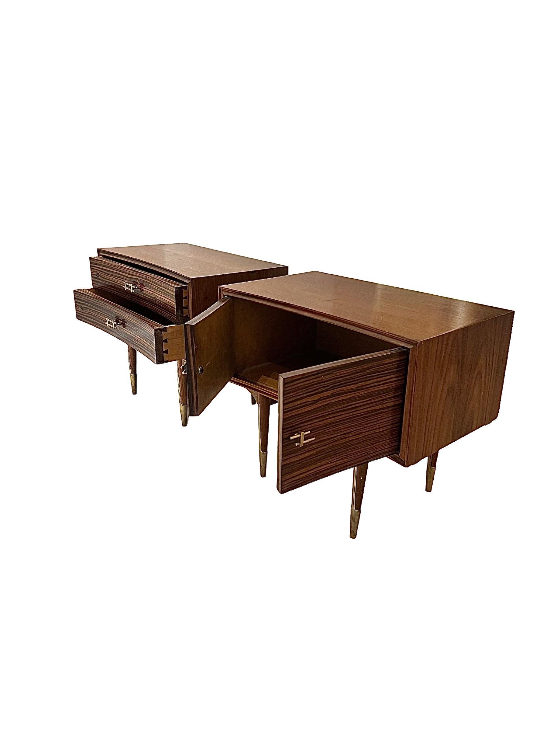 Presenting a striking pair of rosewood nightstands, hailing from the chic era of the 1960s. These elegant pieces are adorned with brass handles, showcasing a timeless fusion of form and function.

Both nightstands share the same graceful shape, yet
