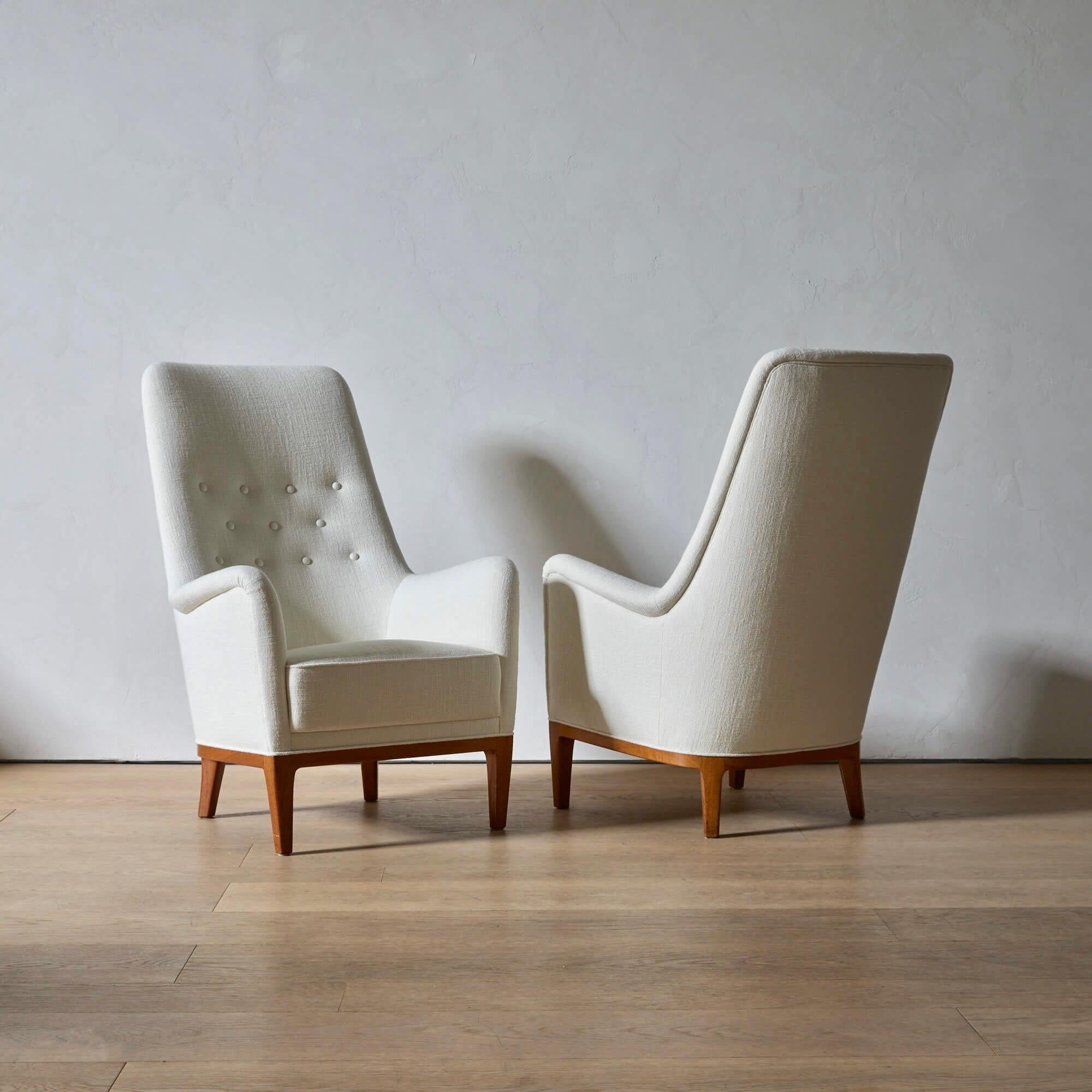 Ein außergewöhnlich bequemes Paar Hochlehner-Sessel, das Mitte des 20. Jahrhunderts von Schwedens renommiertem Luxusdesign-Händler Nordiska Kompaniet hergestellt wurde. Neu restauriert und mit elfenbeinfarbenem Leinen von Manuel Canovas