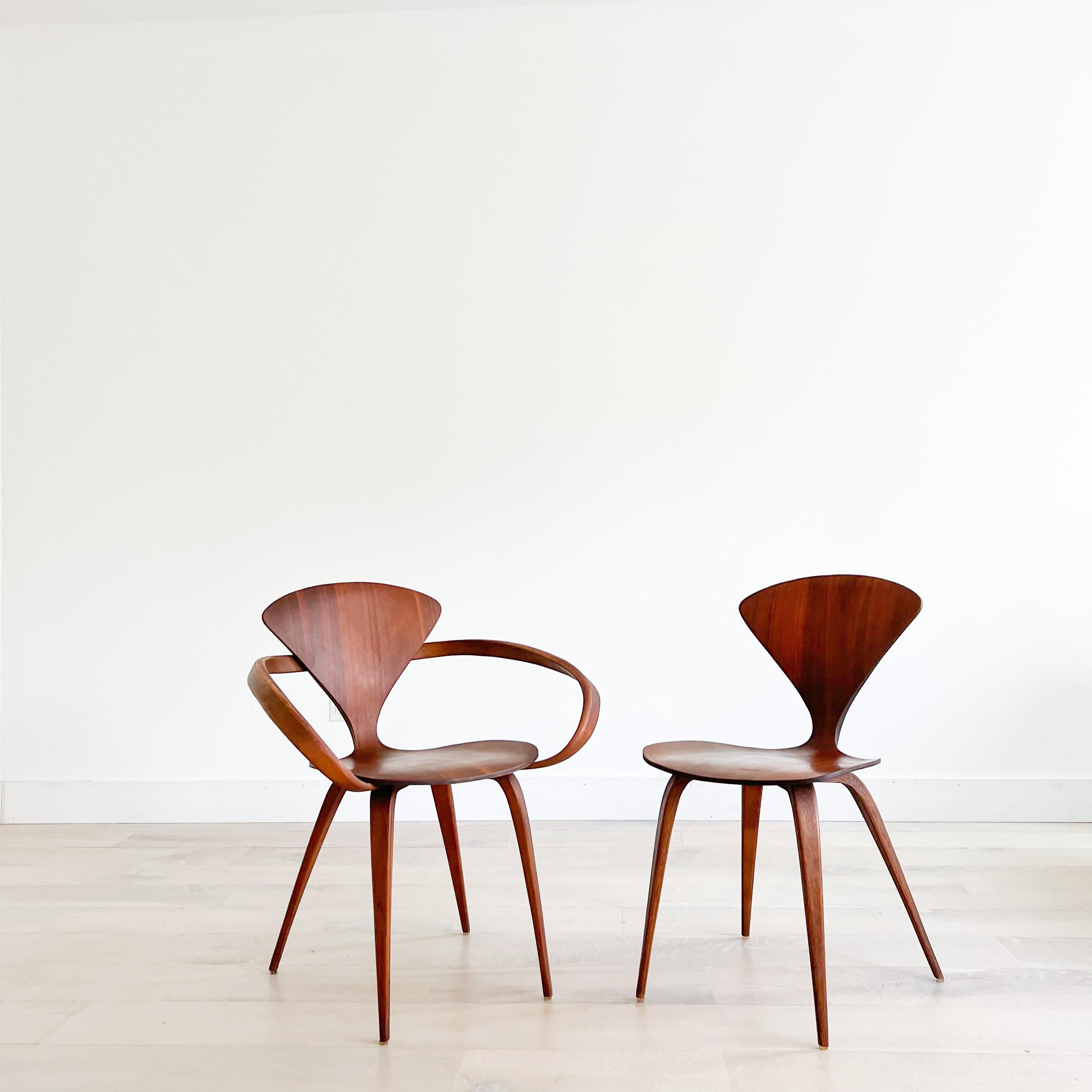 Pair of “pretzel” walnut chairs designed by Norman Cherner for Plycraft. One armless and one armchair. Some light scuffing/scratching/small areas of veneer repair from age appropriate wear.