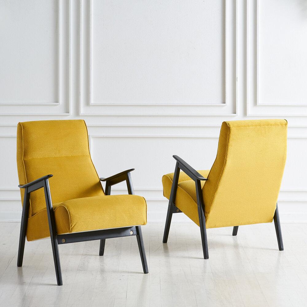 A pair of lounge chairs carefully restored in a vibrant yellow upholstery, sourced in Europe. The wooden frame features a black finish and brass hardware. Ergonomically, these chairs are very comfortable and a beautiful pop of color. 