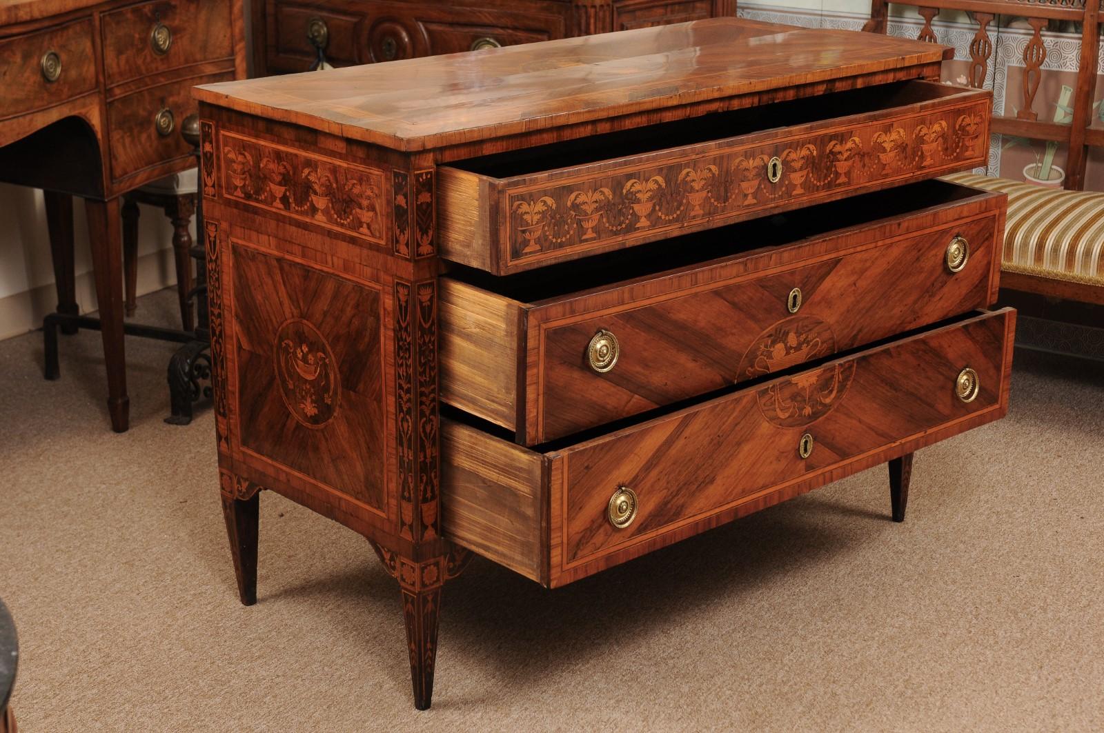 The pair of Northern Italian neoclassical inlaid commodes in tulipwood, rosewood and fruitwood featuring urn and foliate marquetry, cross-banding and string inlay. The commode with 3 drawers and square tapering legs.