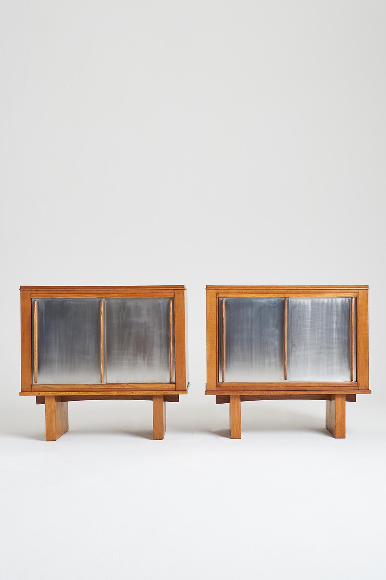 A pair of oak cabinets, in the manner of Charlotte Perriand, the sliding aluminium doors with shaped handles revealing central shelves.
France, Circa 1950.