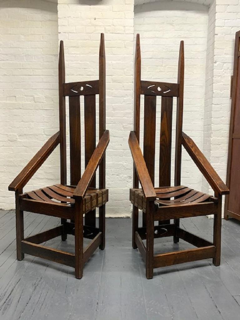An early pair of 20th century Mission, oak armchairs, with leather strap seats, sloping arms and wide four sided stretchers. Has a slatted back.